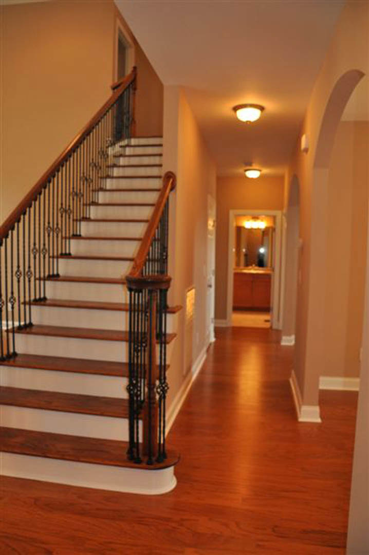 Wood staircase with white balusters and handrail, set on light hardwood flooring in a hallway with neutral walls and a modern ceiling light fixture