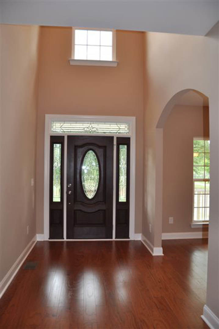 Hardwood floor with sunlight reflecting, white paneled wall, wooden door with glass inset, adjacent window framed by wood molding