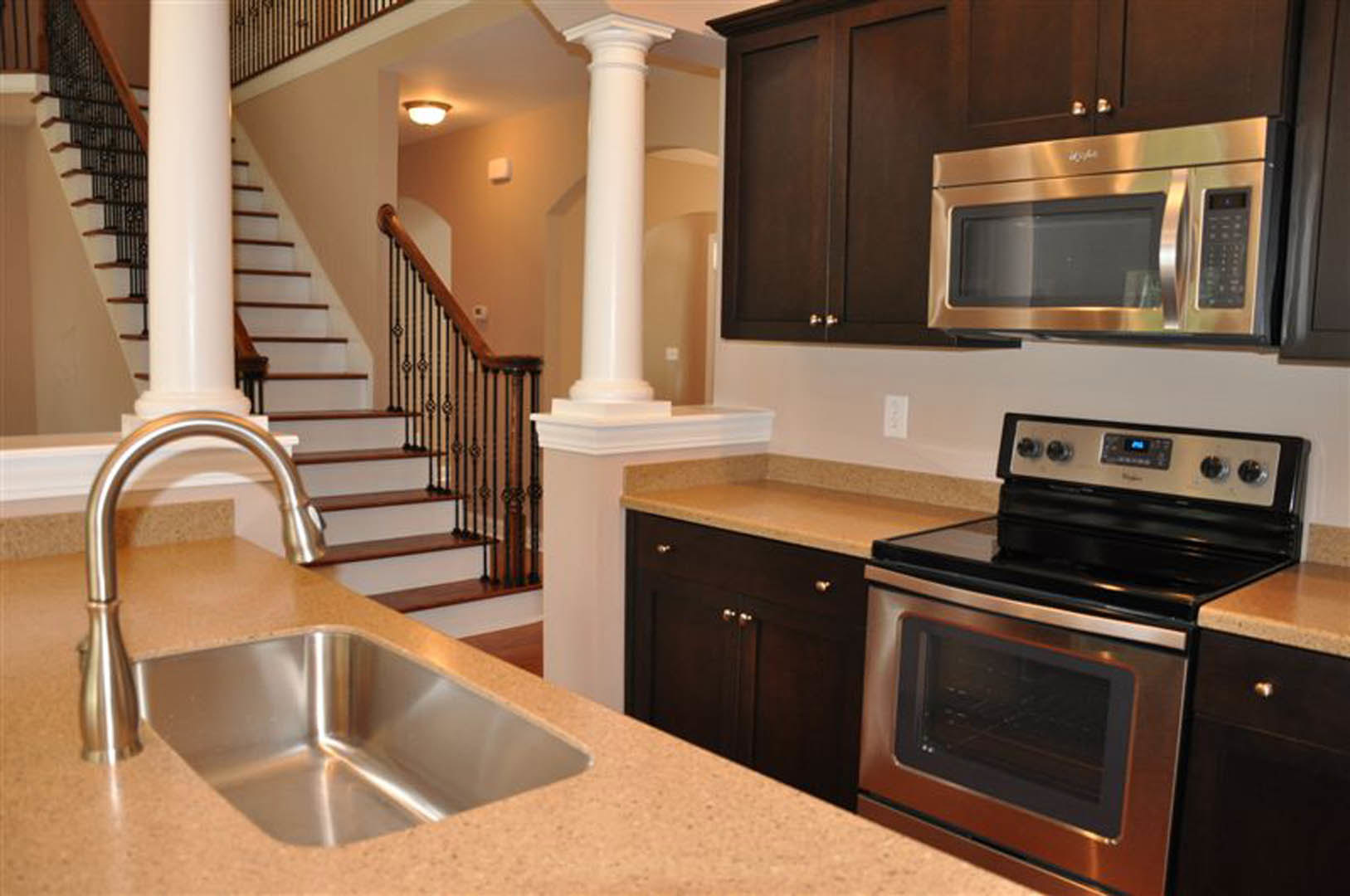 Open kitchen with white cabinetry, stainless steel stove and oven, built-in microwave, undermount sink, stone countertops, wood staircase with metal railing, and modern ceiling