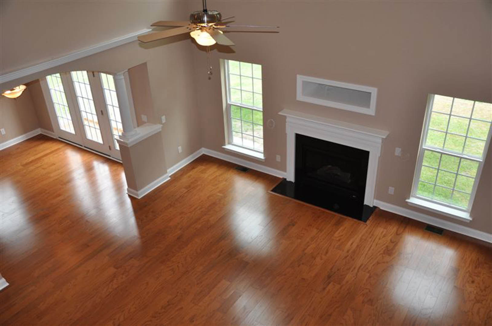 Living room with hardwood floors, stone fireplace, large window overlooking grassy field, white walls, and minimalist decor