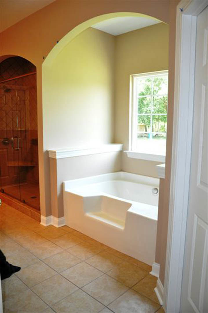 White freestanding bathtub with step in corner, multi-pane window, tile floor, and hardwood cabinetry in bathroom