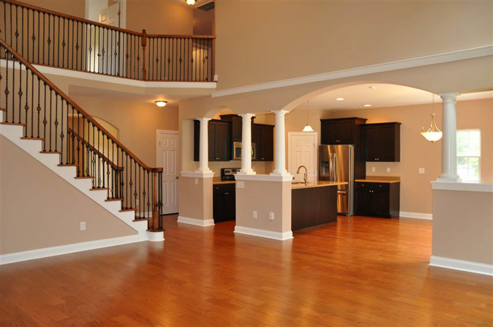 Open-concept kitchen with black cabinets and wooden countertops, hardwood flooring, white walls, and a metal-railed staircase leading to an upper level