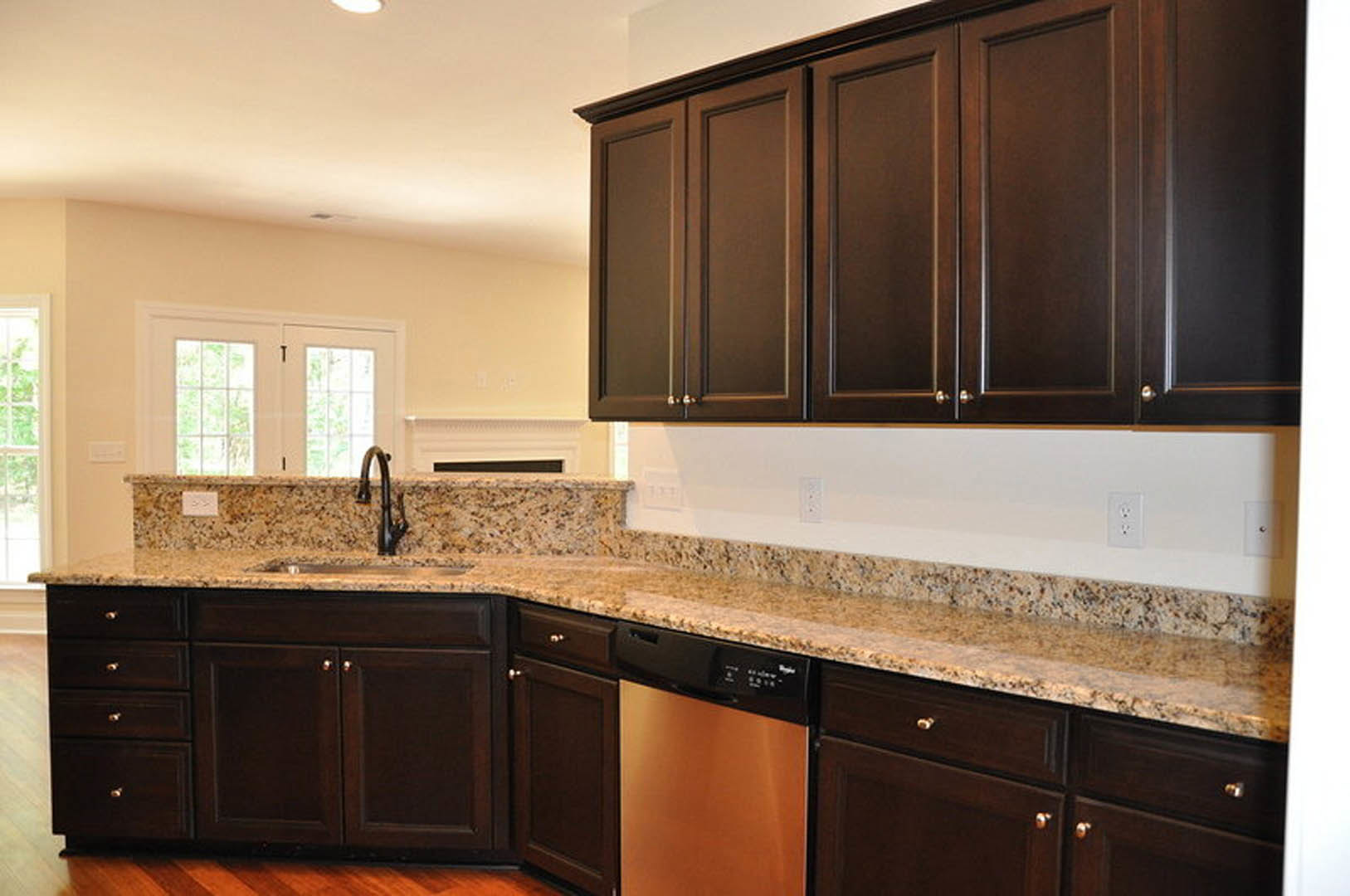 Granite countertops with tile backsplash, white cabinetry, stainless steel faucet, built-in dishwasher, and close-up views of cabinet doors and electrical outlet