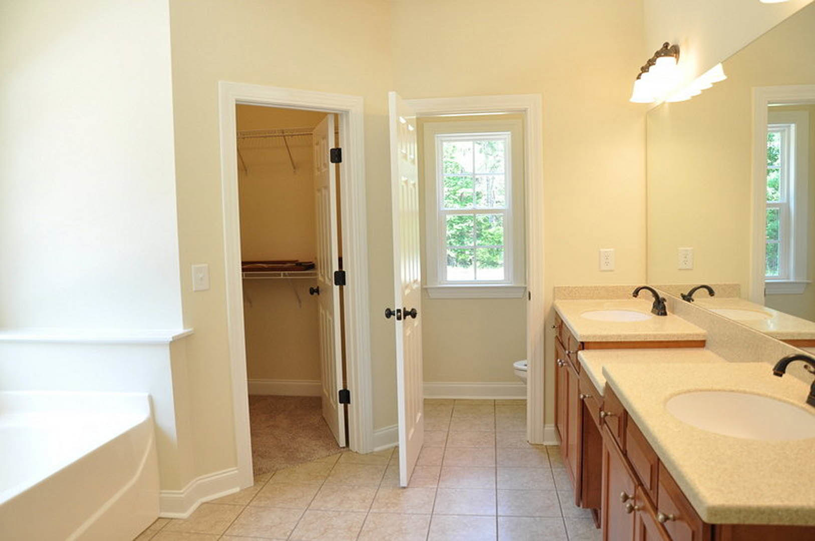 Modern bathroom with white tile floors, freestanding bathtub, sleek vanity sink, large mirror, and window overlooking trees