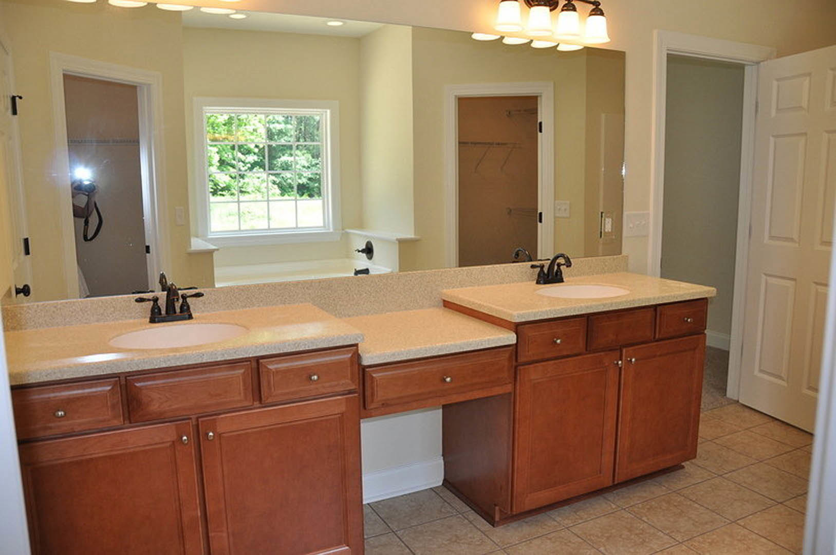 Bathroom with double sinks on a white countertop, black faucets, white cabinetry, tiled walls, large window with multiple panes, glass shower door, and white interior door.