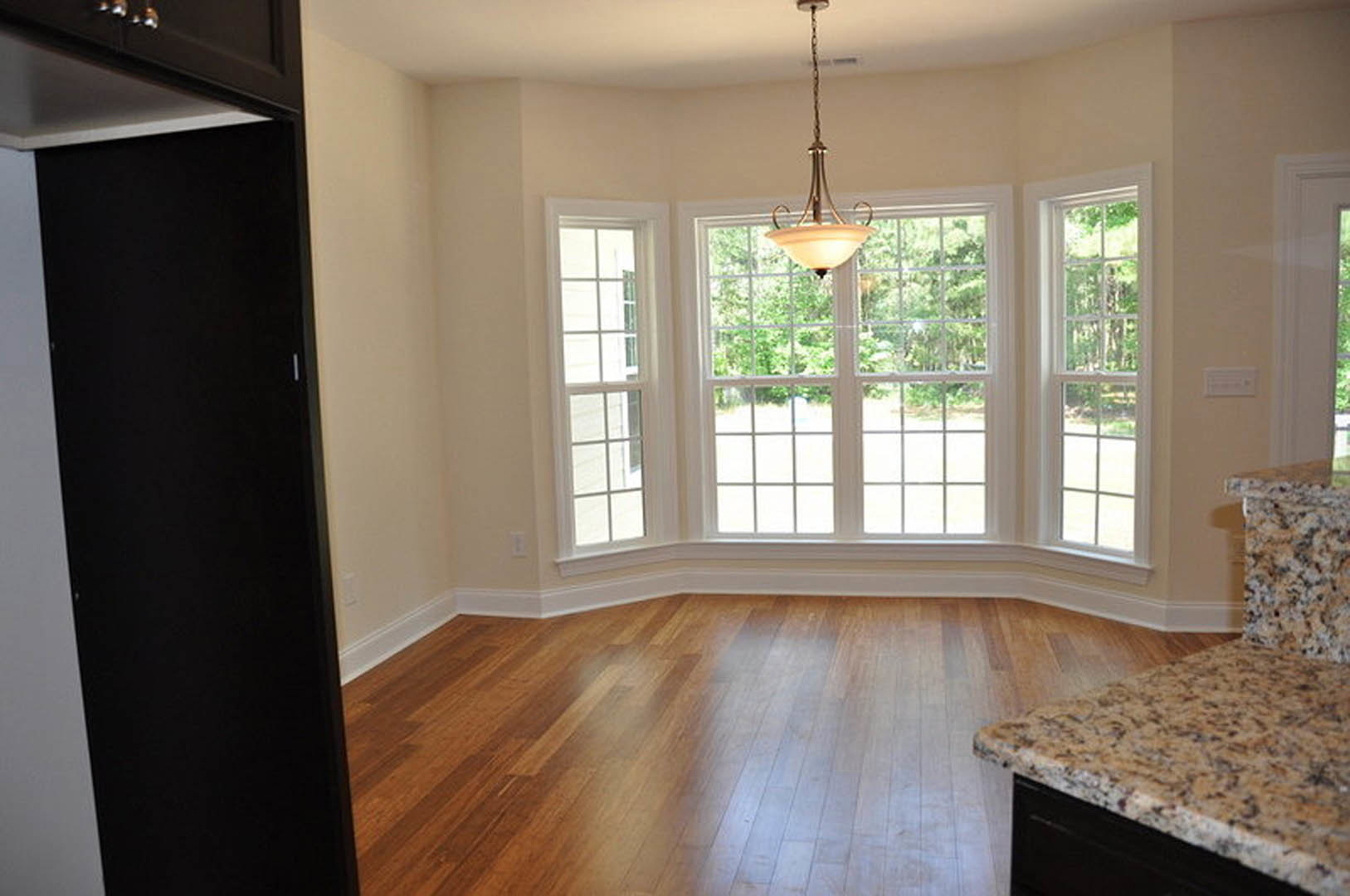 Spacious room featuring a large window with abundant daylight, marble countertop, ceiling light fixture, black rectangular wall accent, and wood laminate flooring.