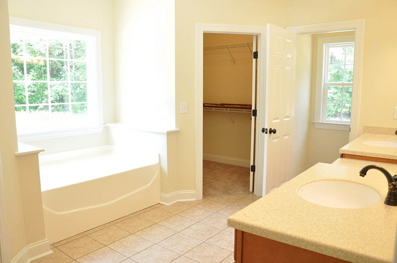 Modern bathroom featuring a freestanding white bathtub, rectangular countertop with integrated sink, chrome faucet, large wall mirror, and light gray tile flooring.