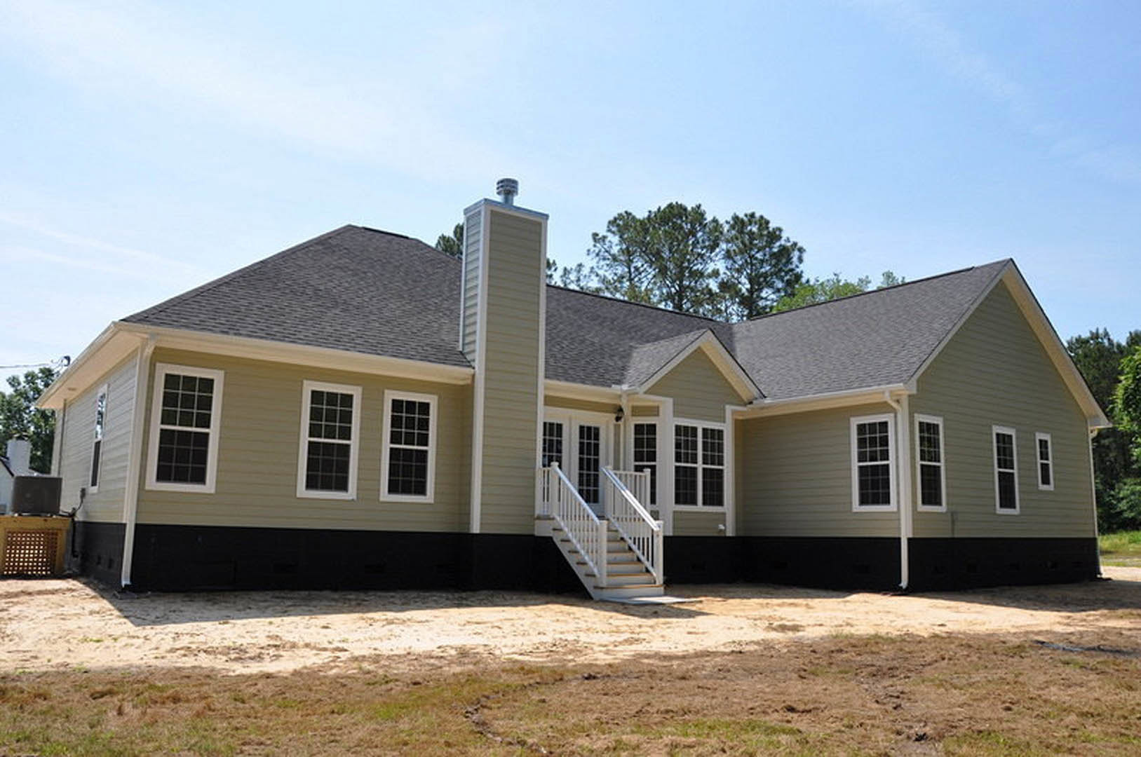 White exterior staircase leads to porch of modern home with light siding, white-framed windows, and chimney; dirt patch and tree visible in front yard.