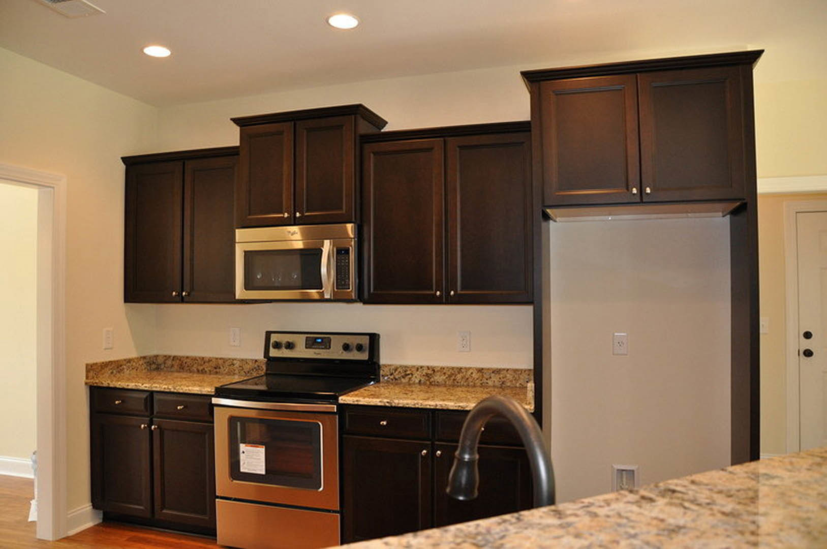 Kitchen with dark wood cabinets, granite countertops, stainless steel stove and microwave, chrome faucet, white wall with light switch, white paper on black counter