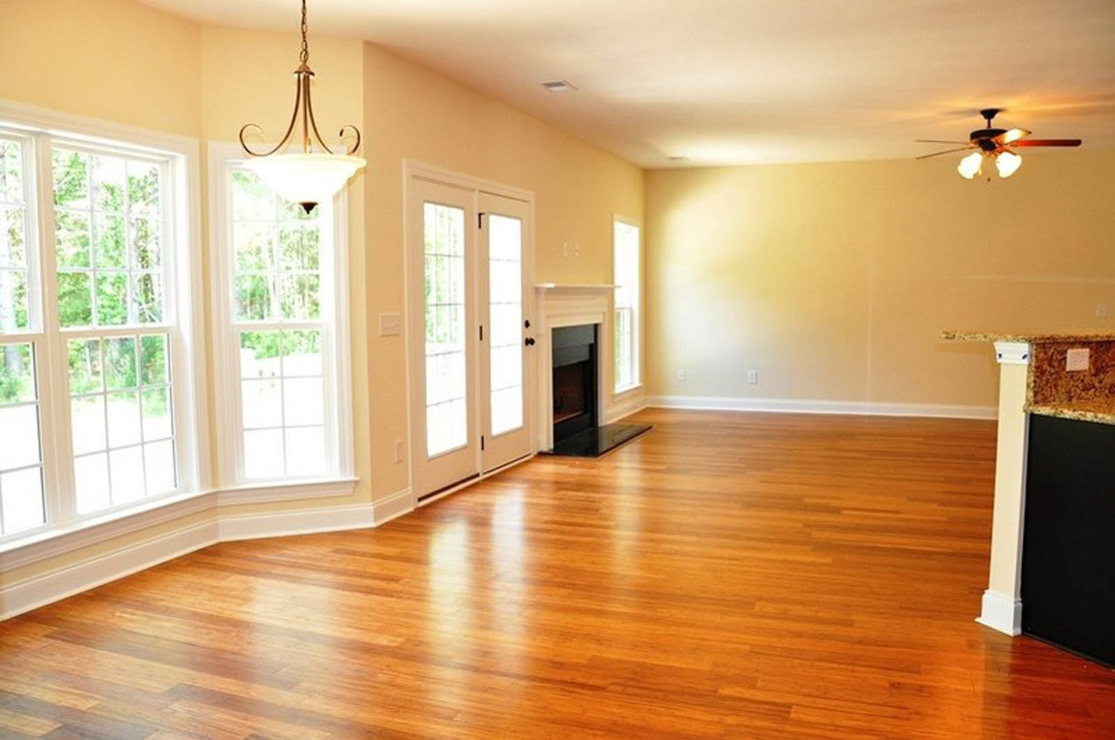 Hardwood floor living area featuring a white fireplace, multi-pane windows, glass-paneled doors, ceiling fan with light, and chandelier