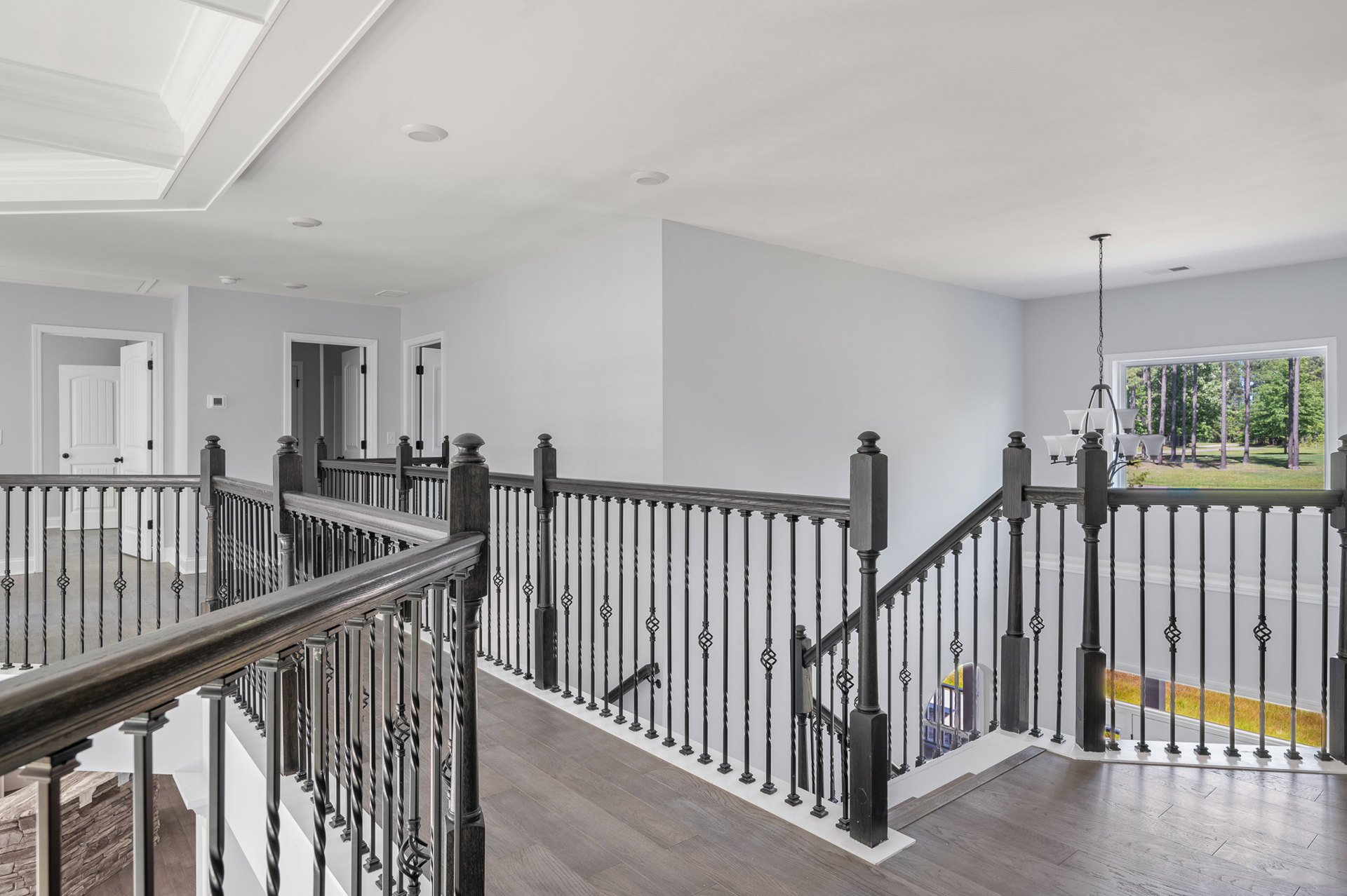 Wood staircase with matte black metal railings, white walls, and a nearby doorway; close-up view of railing and pillar details.