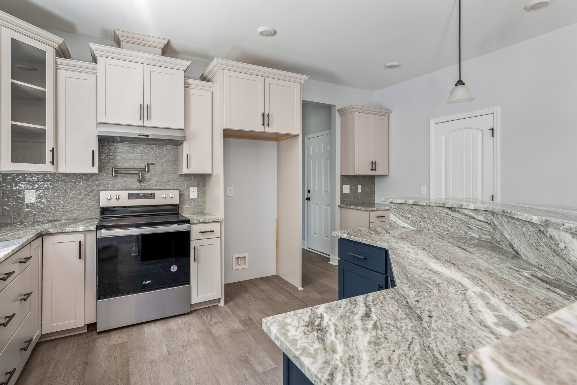 Marble kitchen countertop with white cabinetry featuring black handles, stainless steel oven, and close-up of drawer against a white wall