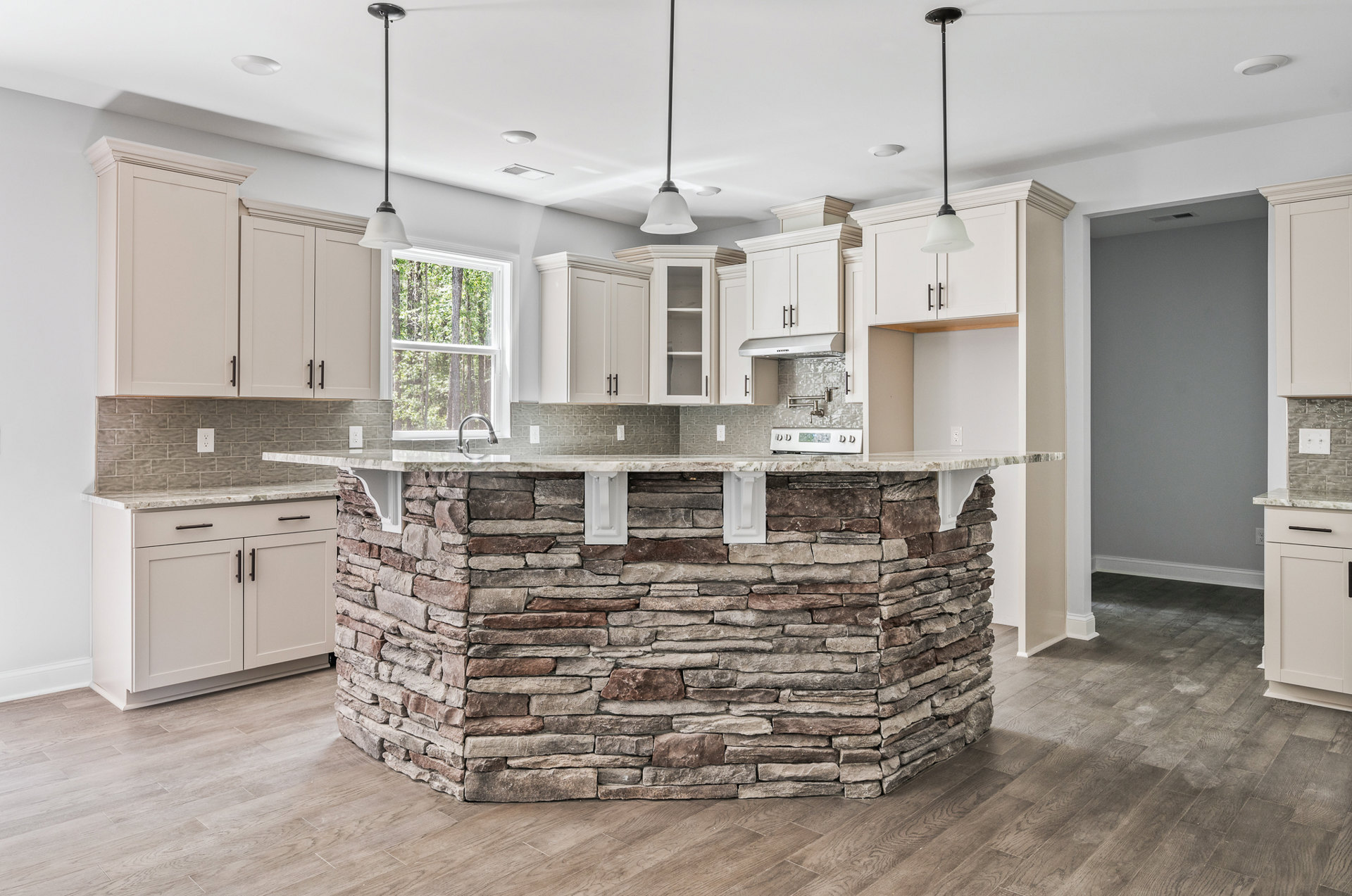 Open-concept kitchen featuring a stone island with marble countertop, built-in sink and faucet, white cabinetry, pendant light fixture, and light hardwood flooring.