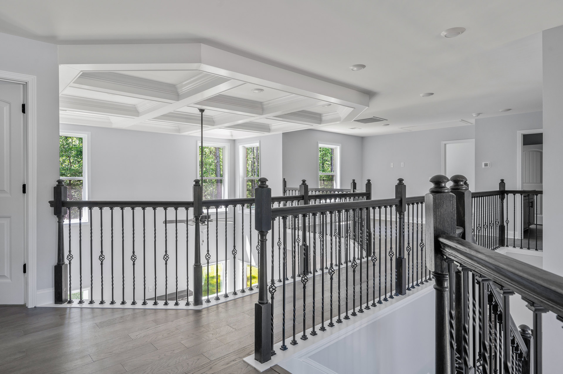 White-walled room featuring a black metal railing, light wood flooring, staircase, and large window overlooking trees
