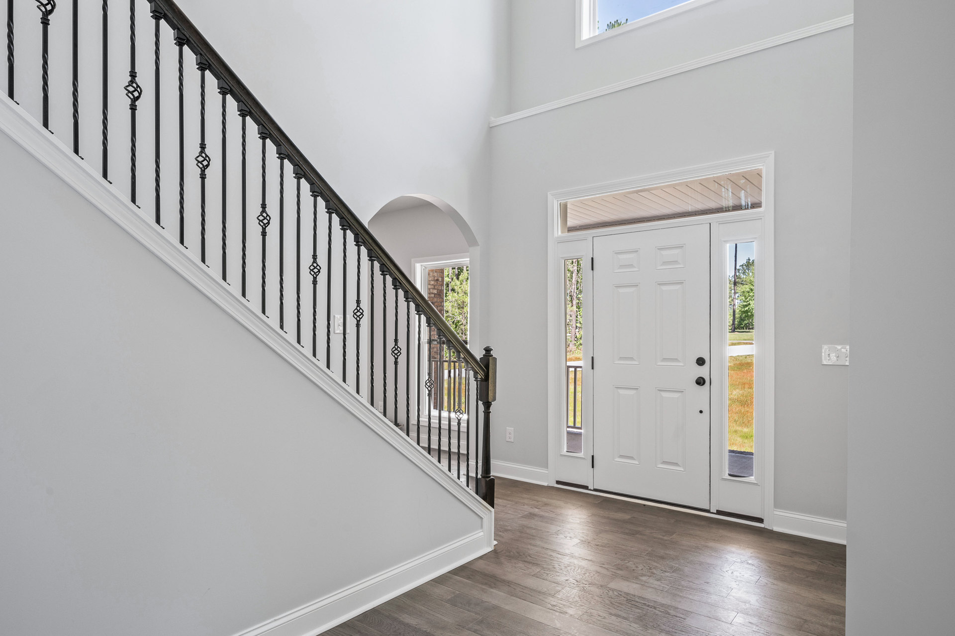 Hardwood staircase with black metal railings, white trim, ceiling light fixture, white door with black knobs and window, plaster walls