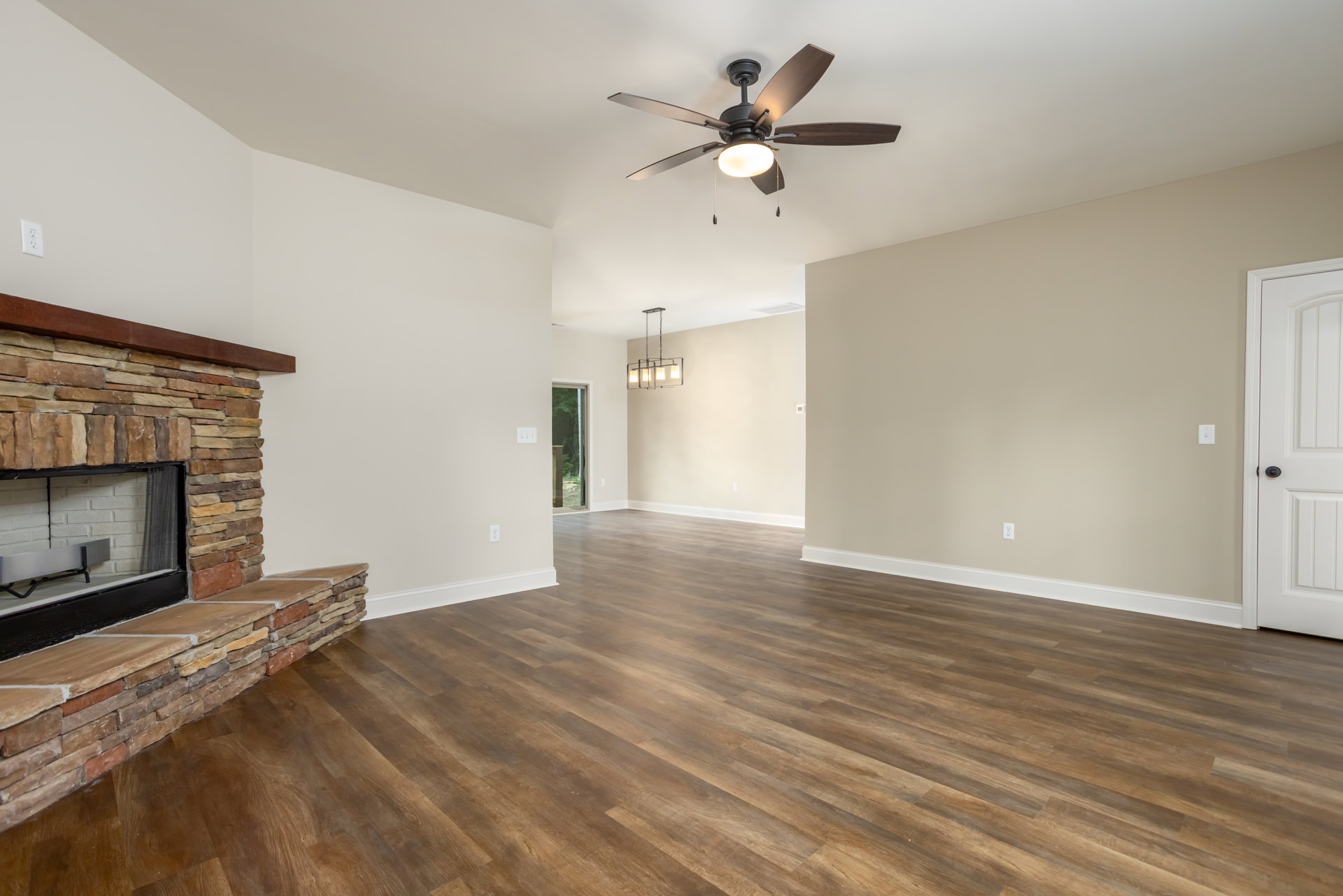Living room with wood flooring, white walls, ceiling fan with light fixture, white door with black handle, and fireplace