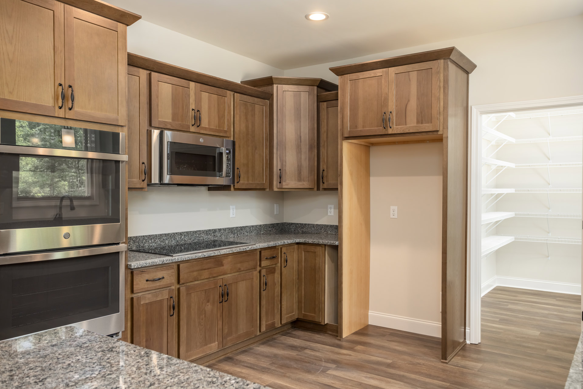 Kitchen featuring wooden cabinets, granite countertops, stainless steel microwave and oven, chrome faucet, and white shelving closet in the background