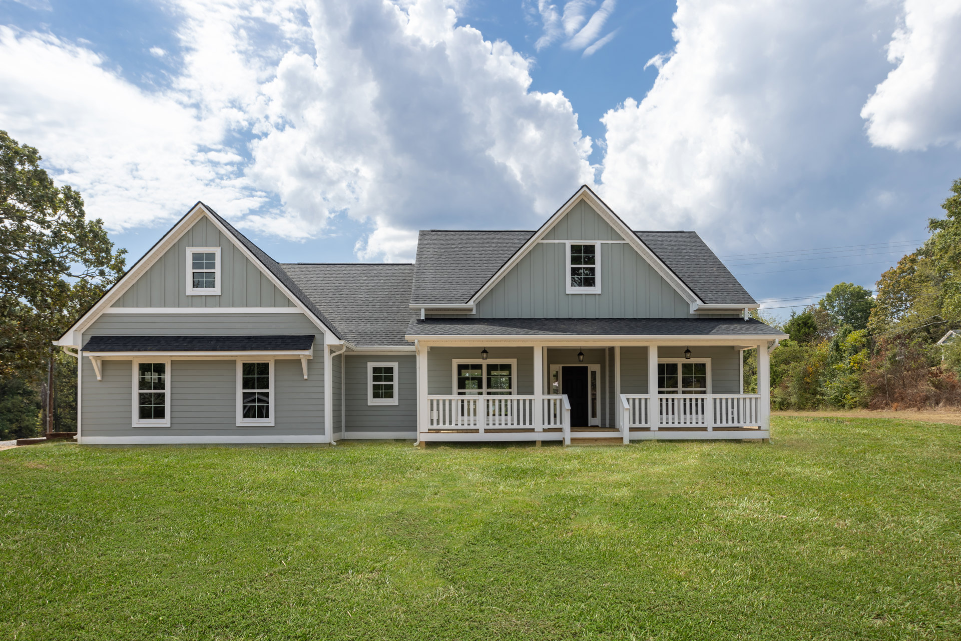 Two-story house with white porch railing, wide lawn, white-framed windows, and Robert Frost Farm visible in the background under a partly cloudy sky