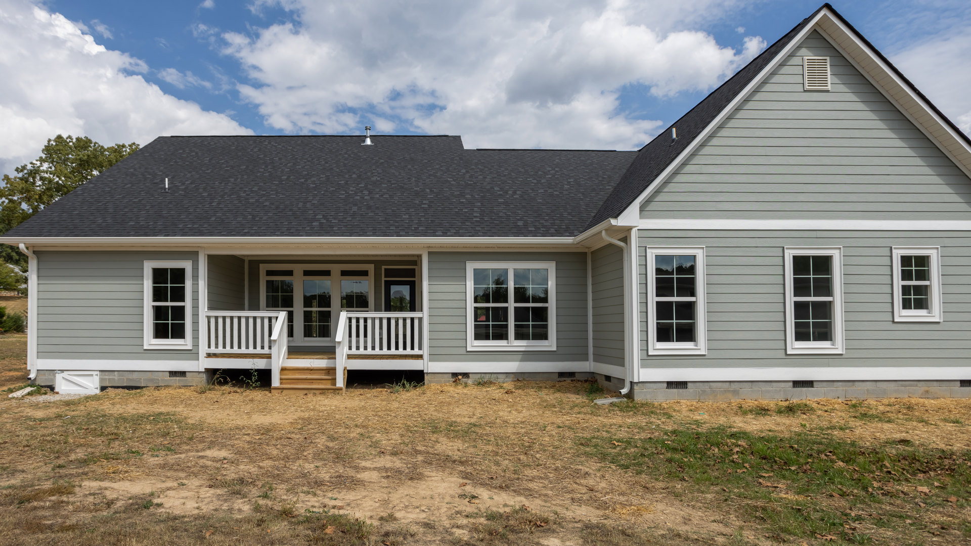 Two-story home with light siding, white-trimmed windows, brick porch steps, grassy yard, and blue sky with scattered clouds