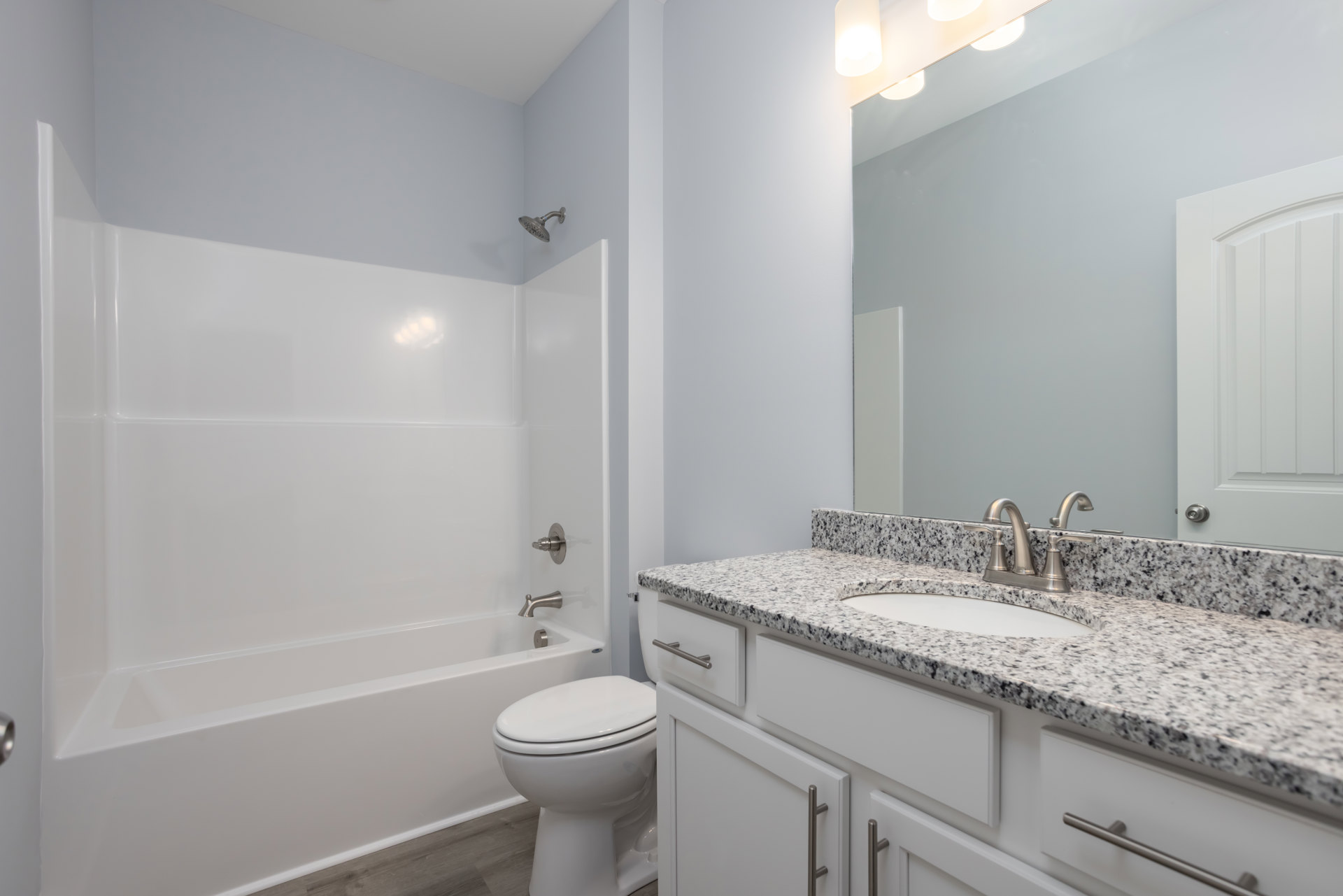 Modern bathroom with white tile walls, undermount sink set in a stone countertop, chrome faucet, frameless mirror, white toilet, and wall-mounted shower head