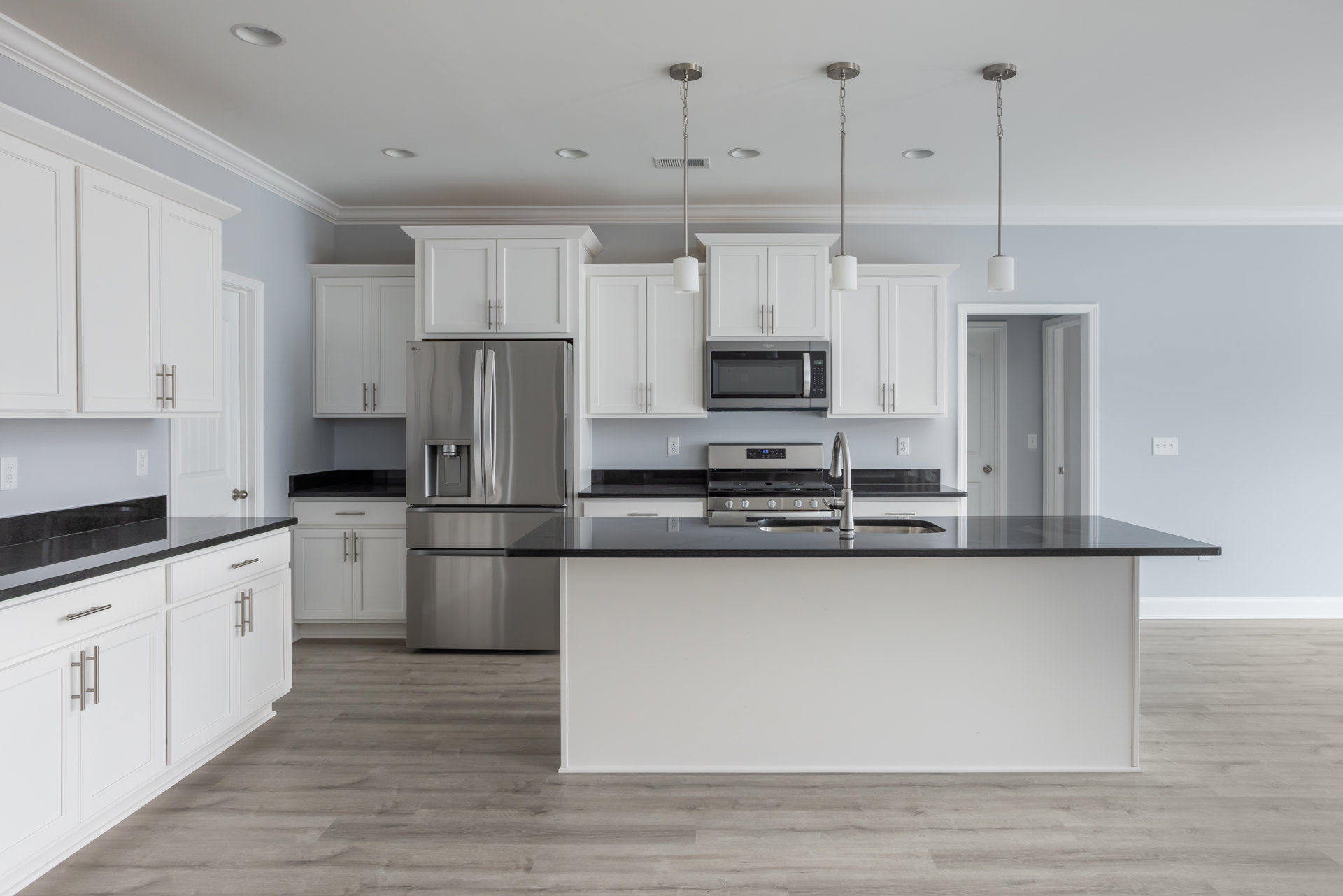 Kitchen with black stone countertop, stainless steel refrigerator with water dispenser, glass door microwave, stove, undermount sink with chrome faucet, white cabinetry, and white