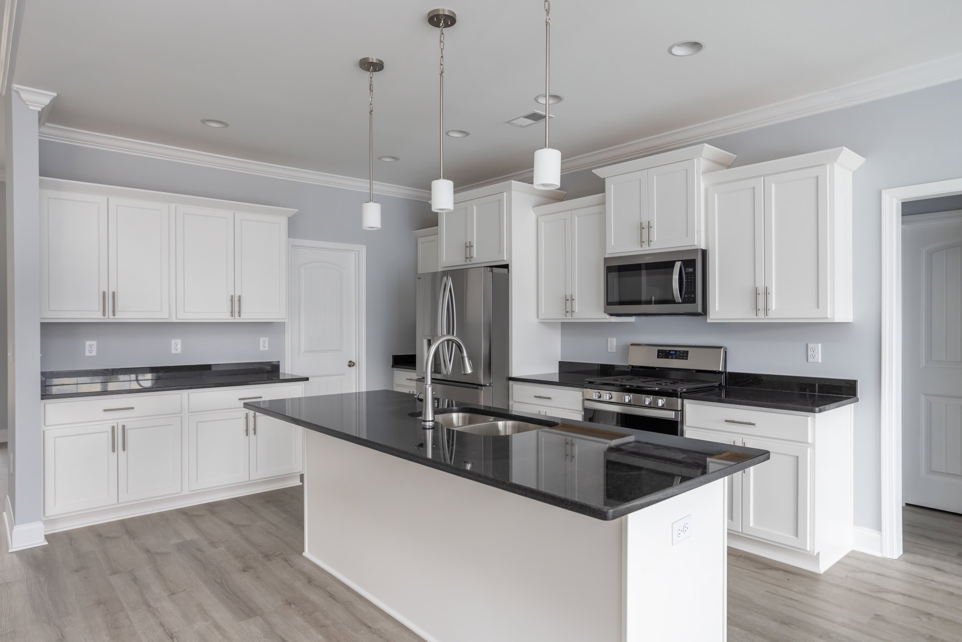 White kitchen cabinets with black countertops, stainless steel microwave, stove, white lamp shade, and white-framed wall.