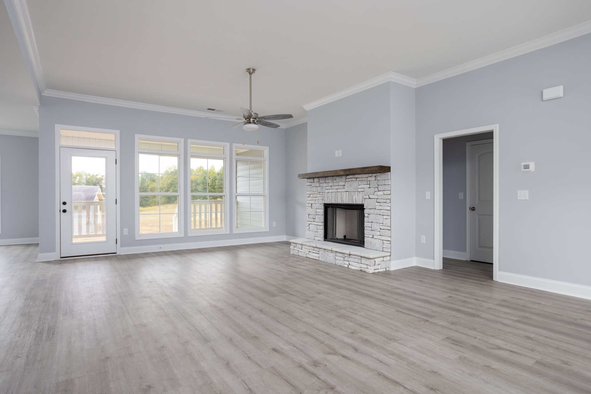 Living room with wood flooring, fireplace featuring a mesh screen and wood mantel, ceiling fan, white door with window, light-colored walls