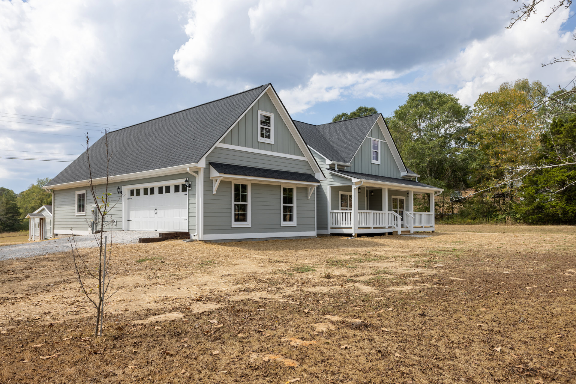 Two-story house with attached garage, grassy front yard, large tree, white porch railing, and white-framed windows under a partly cloudy sky