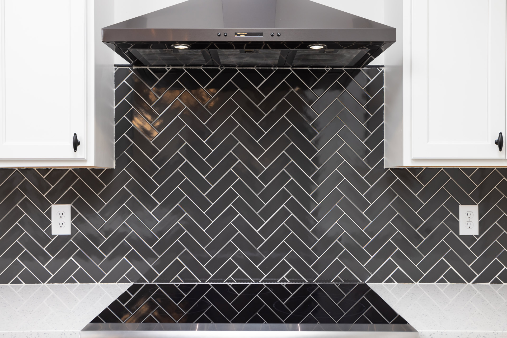 Black range with matching hood, white tile backsplash, light stone countertop, stainless sink, white door with black handle, modern kitchen appliances