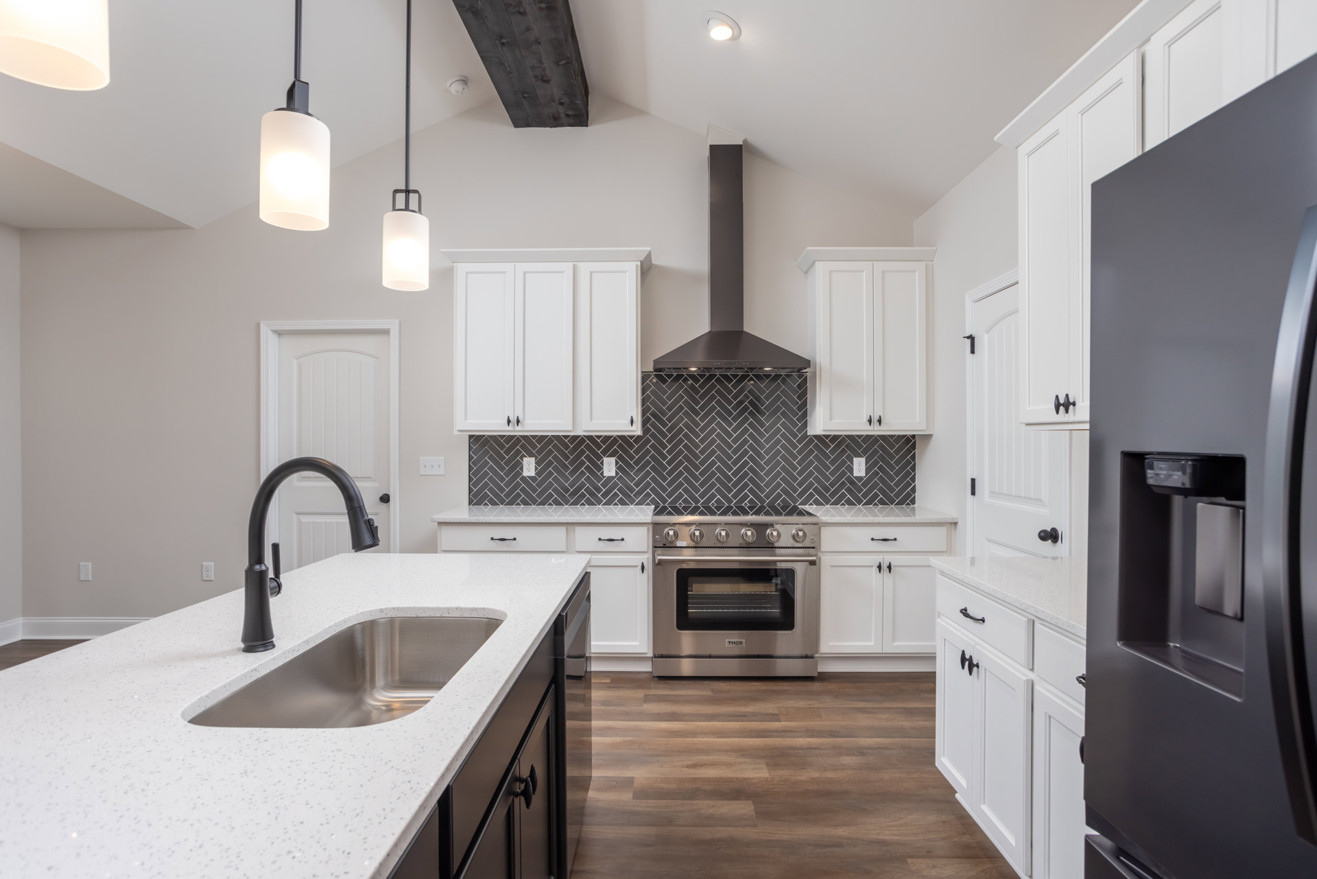 White cabinetry and black appliances in a modern kitchen with stainless steel oven, black tile backsplash, undermount sink with chrome faucet, and contemporary light fixture.