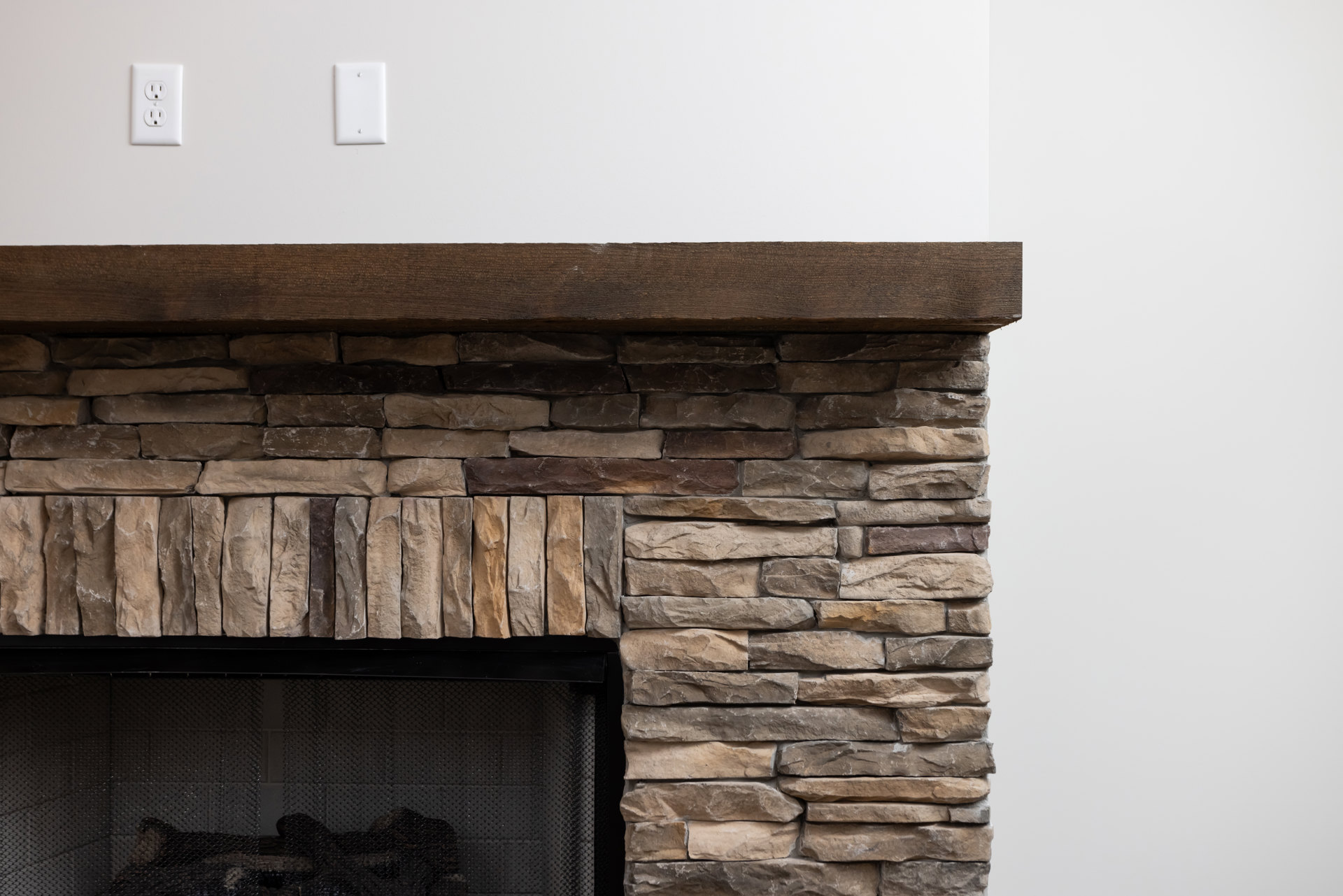 Brick fireplace with wood mantle, black mesh fire screen, and hearth in a residential interior.