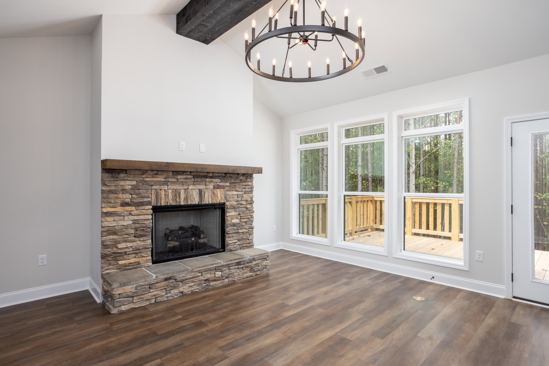 Living room with wood flooring, black mesh fireplace screen, stacked logs in a metal cage, and a multi-light chandelier hanging from the ceiling.