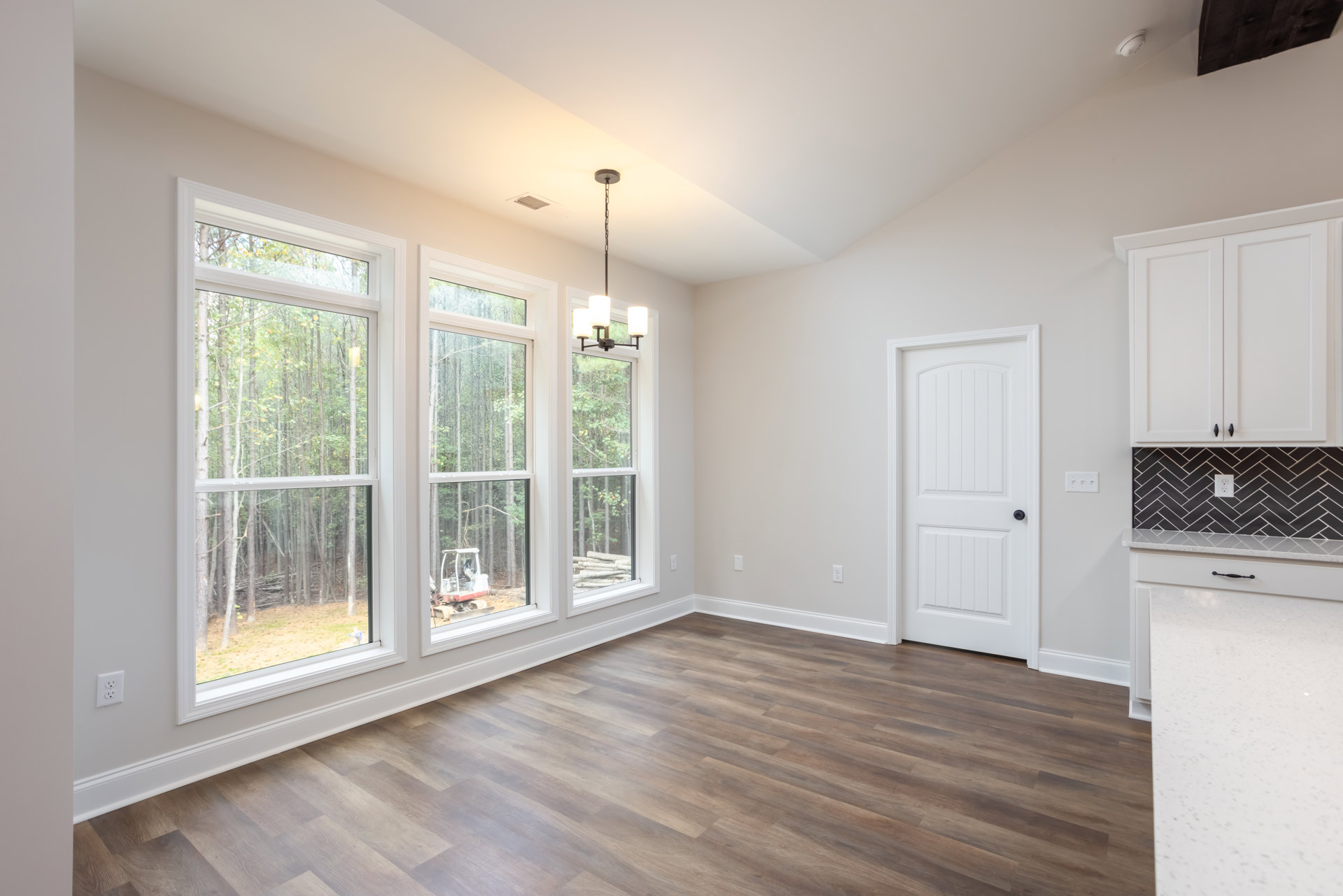 Wood floor room with large windows overlooking trees, white door with black knob, neutral walls, natural light filling the space