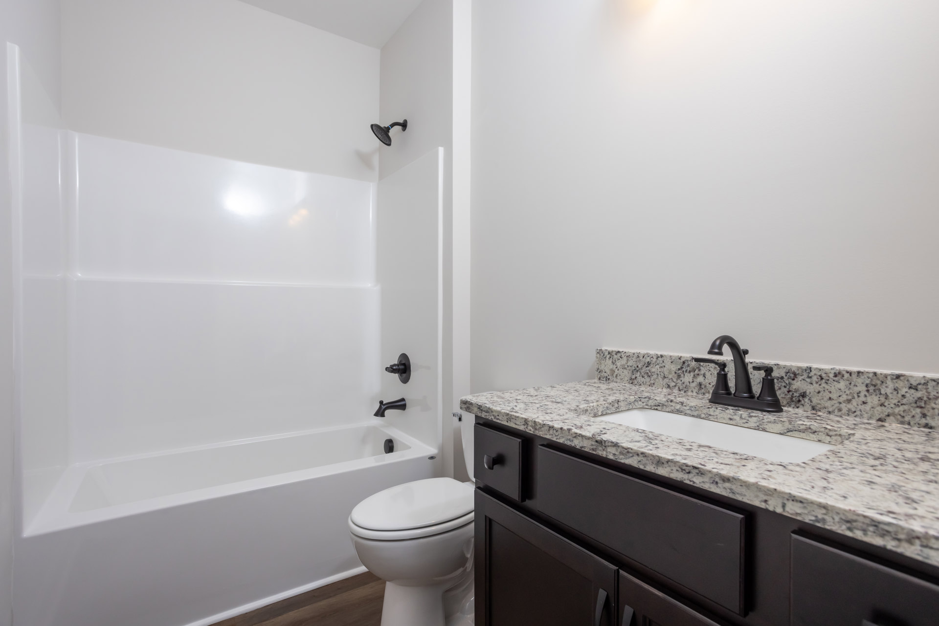 Modern bathroom with white toilet, wall-mounted shower head, black soap dispenser on white countertop, and sink set in light-colored cabinetry with tiled walls.