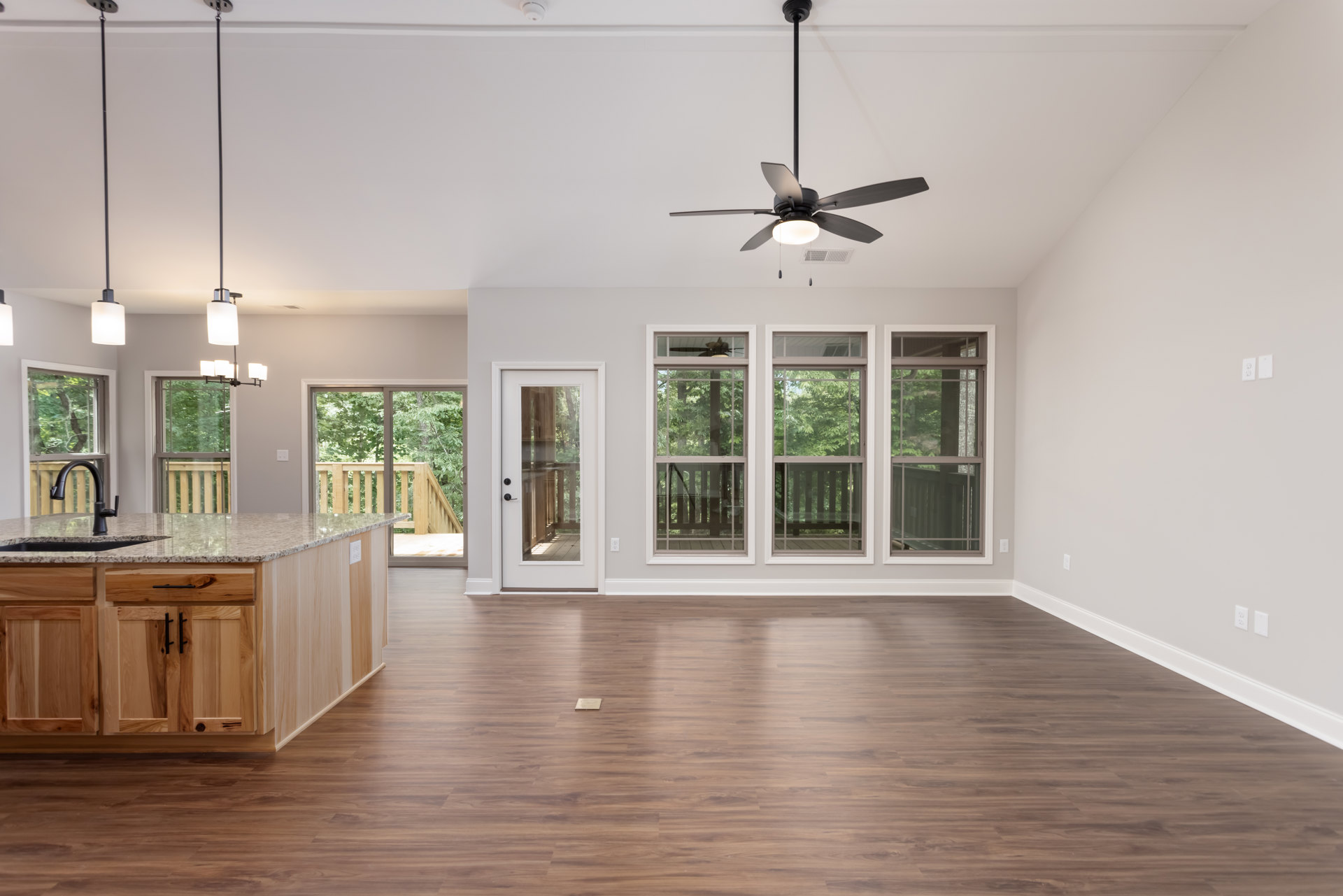 Living room with wood flooring, ceiling fan with light fixture, kitchen island featuring a sink, white door with glass panes, cabinetry, and neutral walls