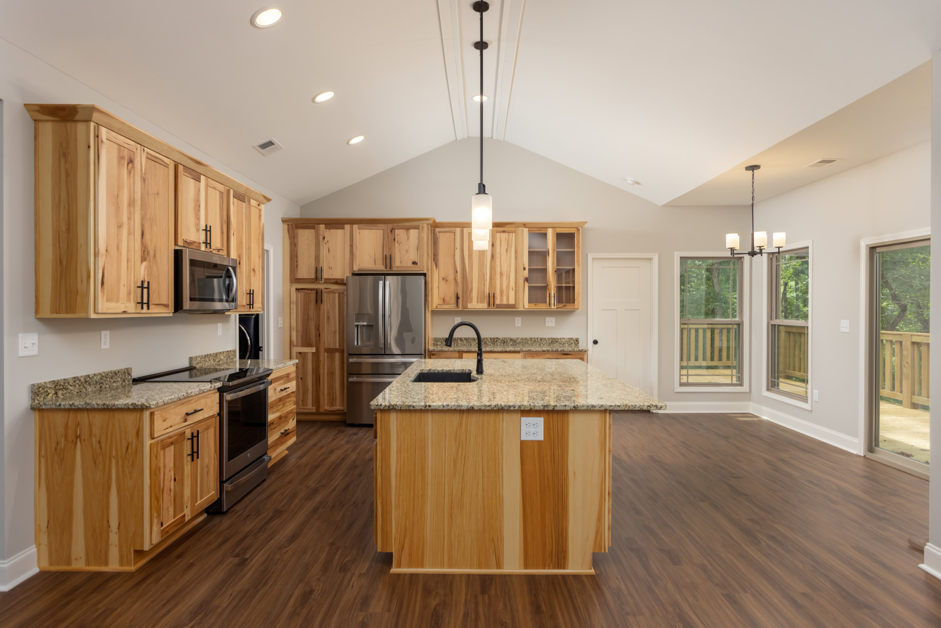 Spacious kitchen featuring a large marble island with built-in sink and black faucet, wood flooring, stainless steel refrigerator, microwave oven, white cabinetry, and window