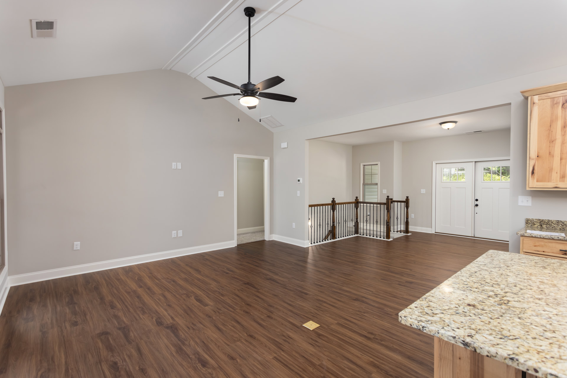 Spacious living room featuring polished wood flooring, marble countertop, ceiling fan with light, white door and door frame, cabinetry, and modern interior finishes