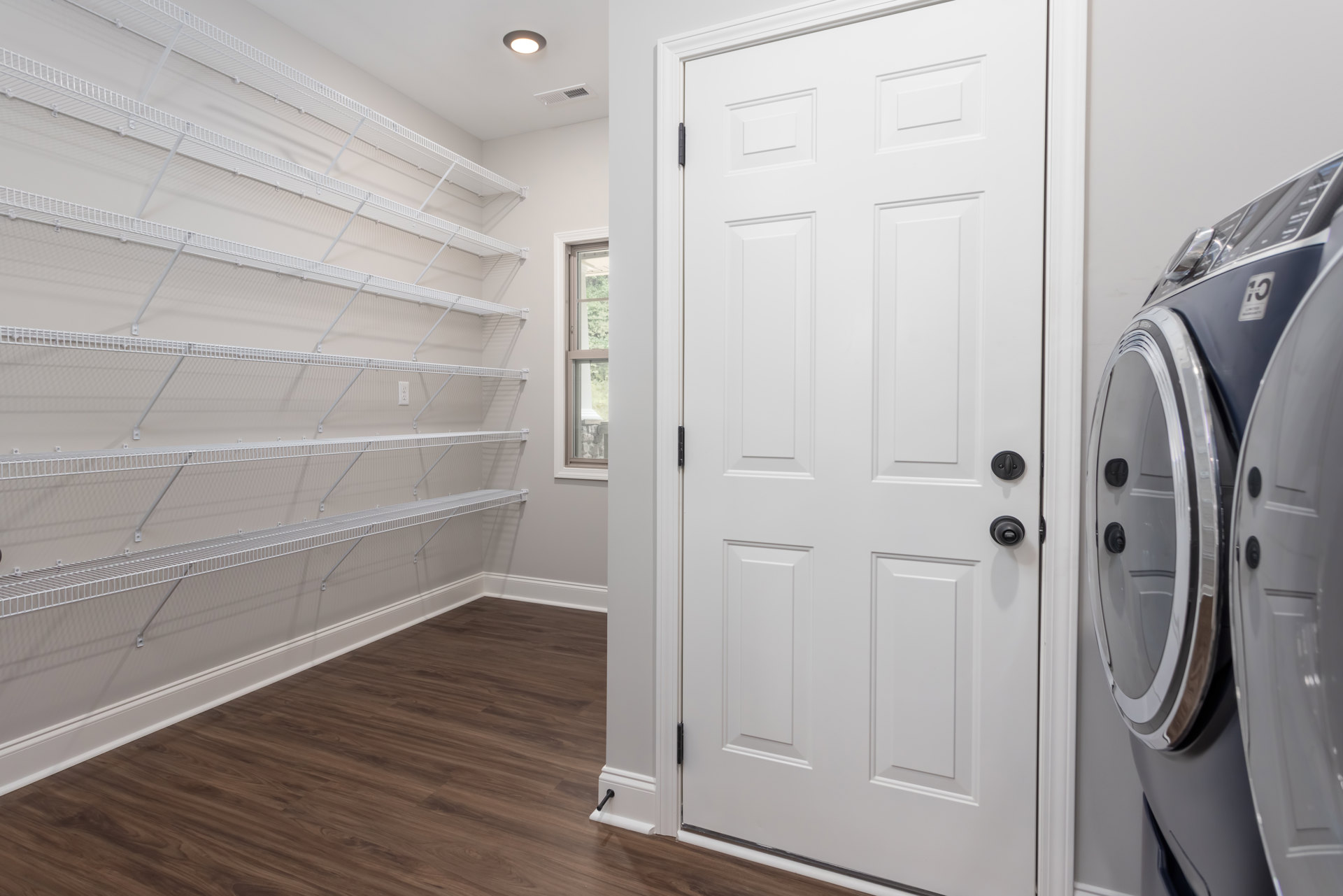White round door with black knobs set in a room featuring built-in white shelves, wood flooring, and white walls.