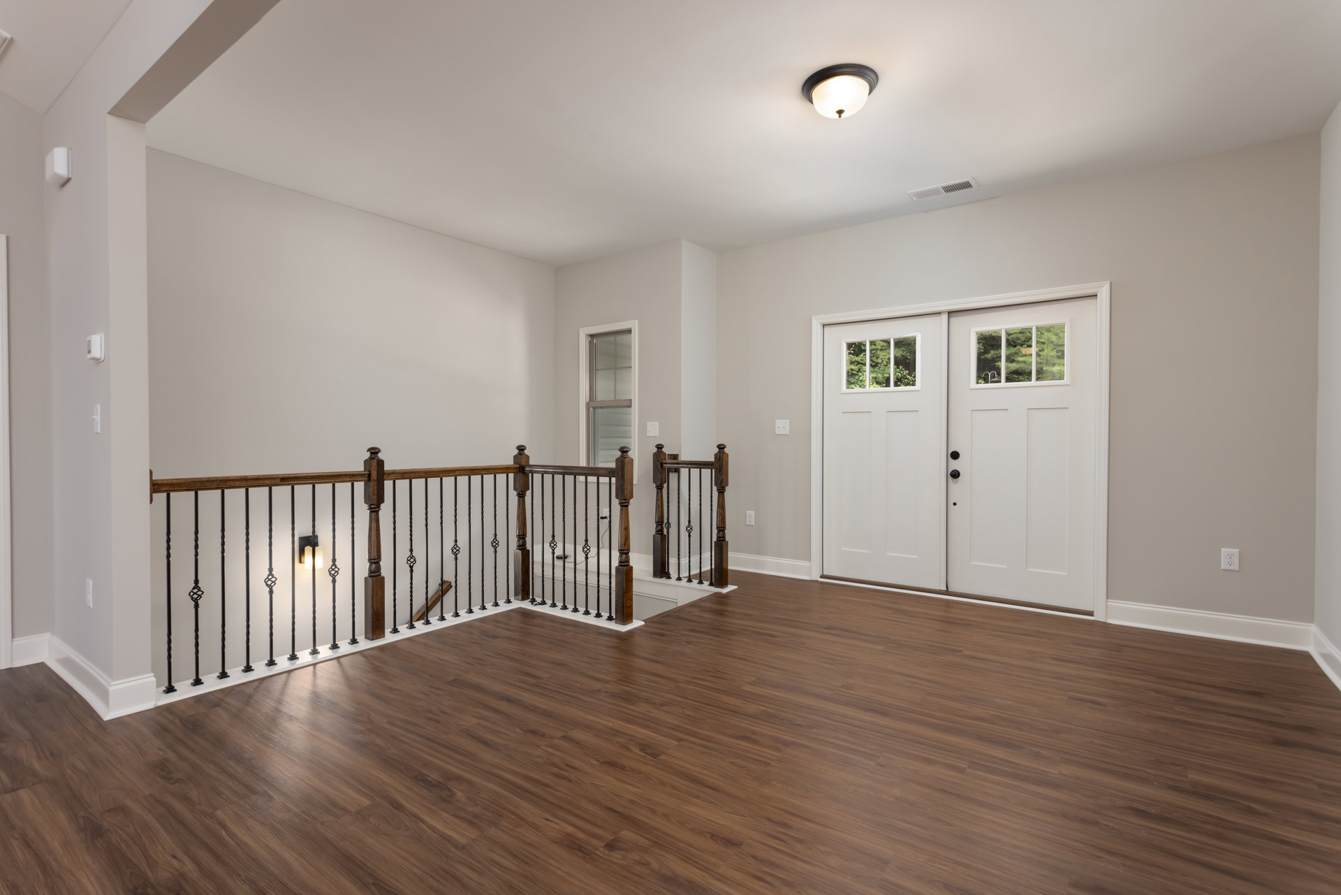 Wood flooring, white plaster walls, wooden railing, ceiling light fixture, double white doors with glass panes