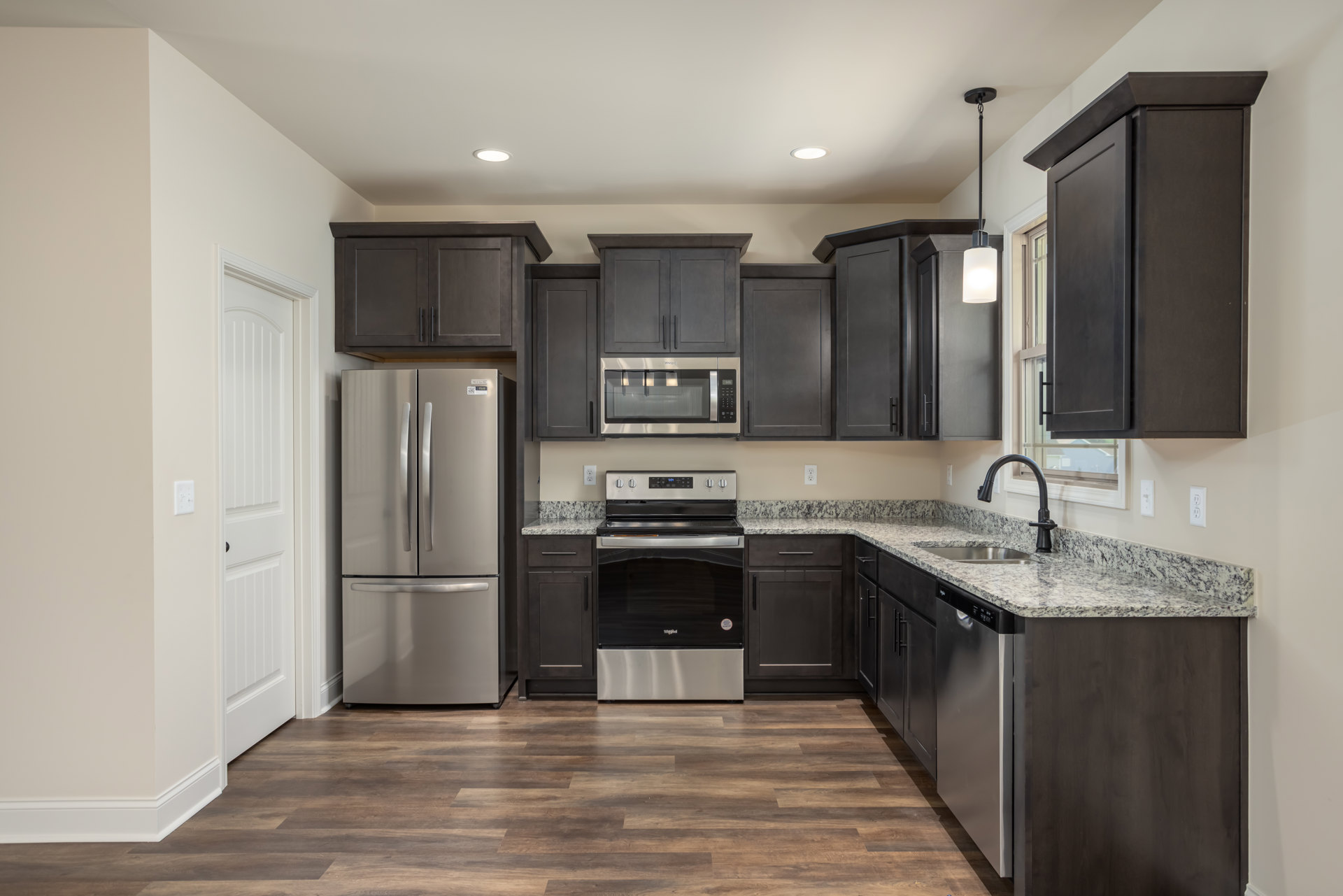 Kitchen with dark wood cabinets, marble countertop, stainless steel refrigerator, black and silver stove, built-in microwave, and modern appliances