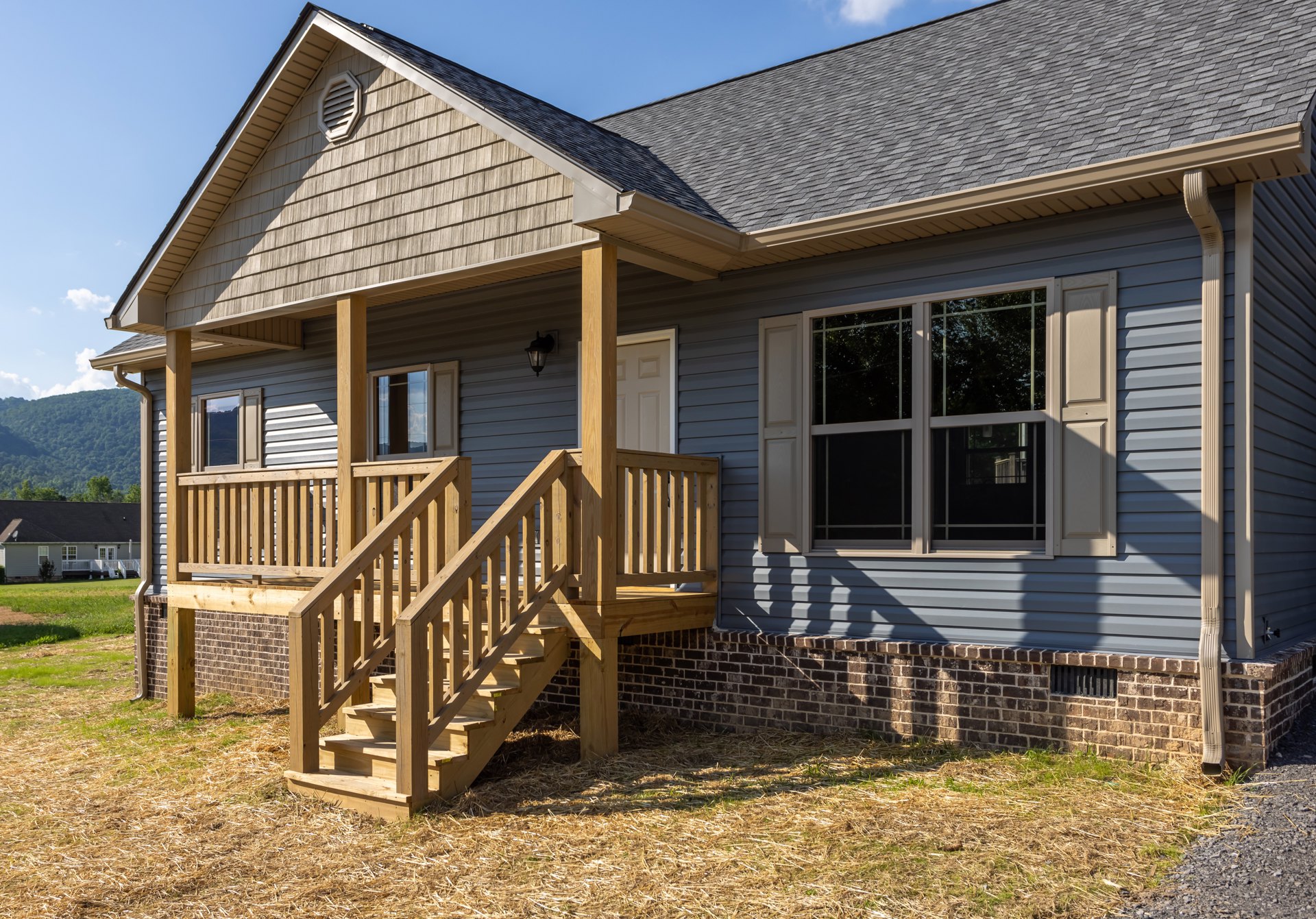 Two-story home with gray siding, white-trimmed windows, covered front porch, wooden stairs, and white railing