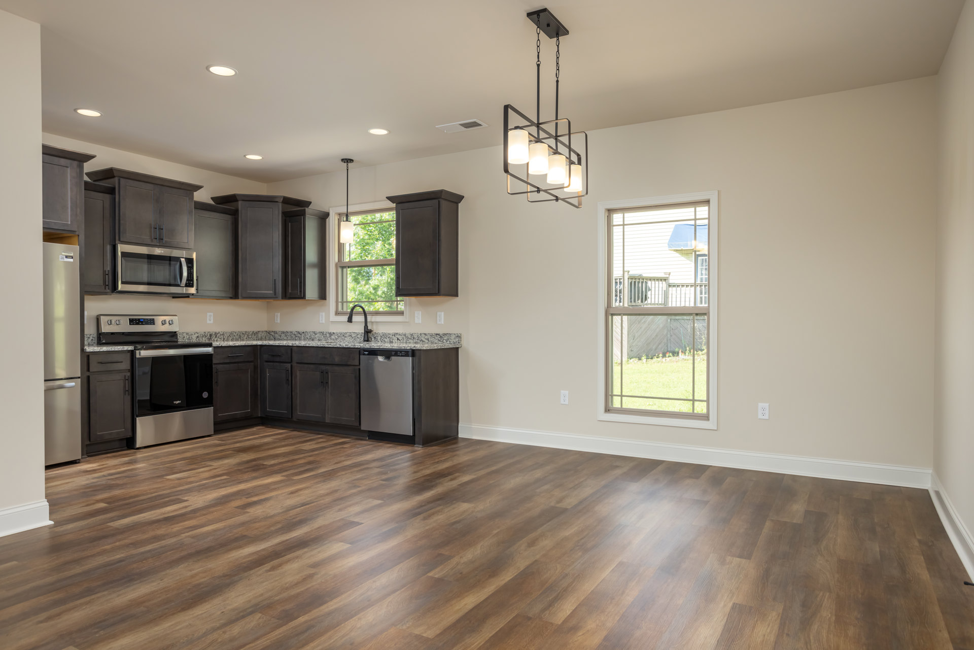 Kitchen with hardwood flooring, wood cabinetry, black refrigerator, open microwave door, stove and oven, ceiling light fixture, window overlooking deck and fence