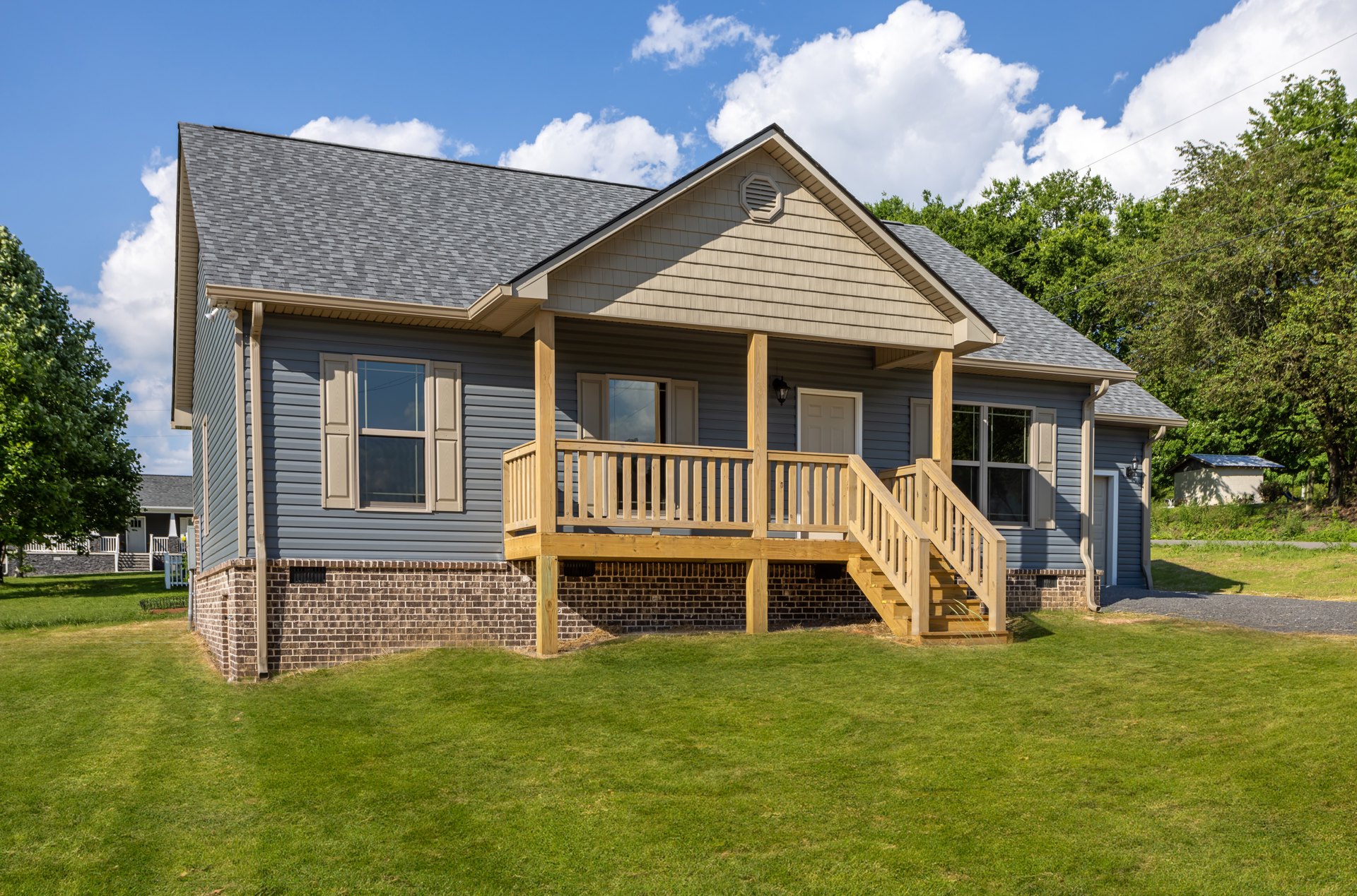 Two-story house with white siding, wooden porch, brick foundation, shuttered windows, and green lawn under partly cloudy sky