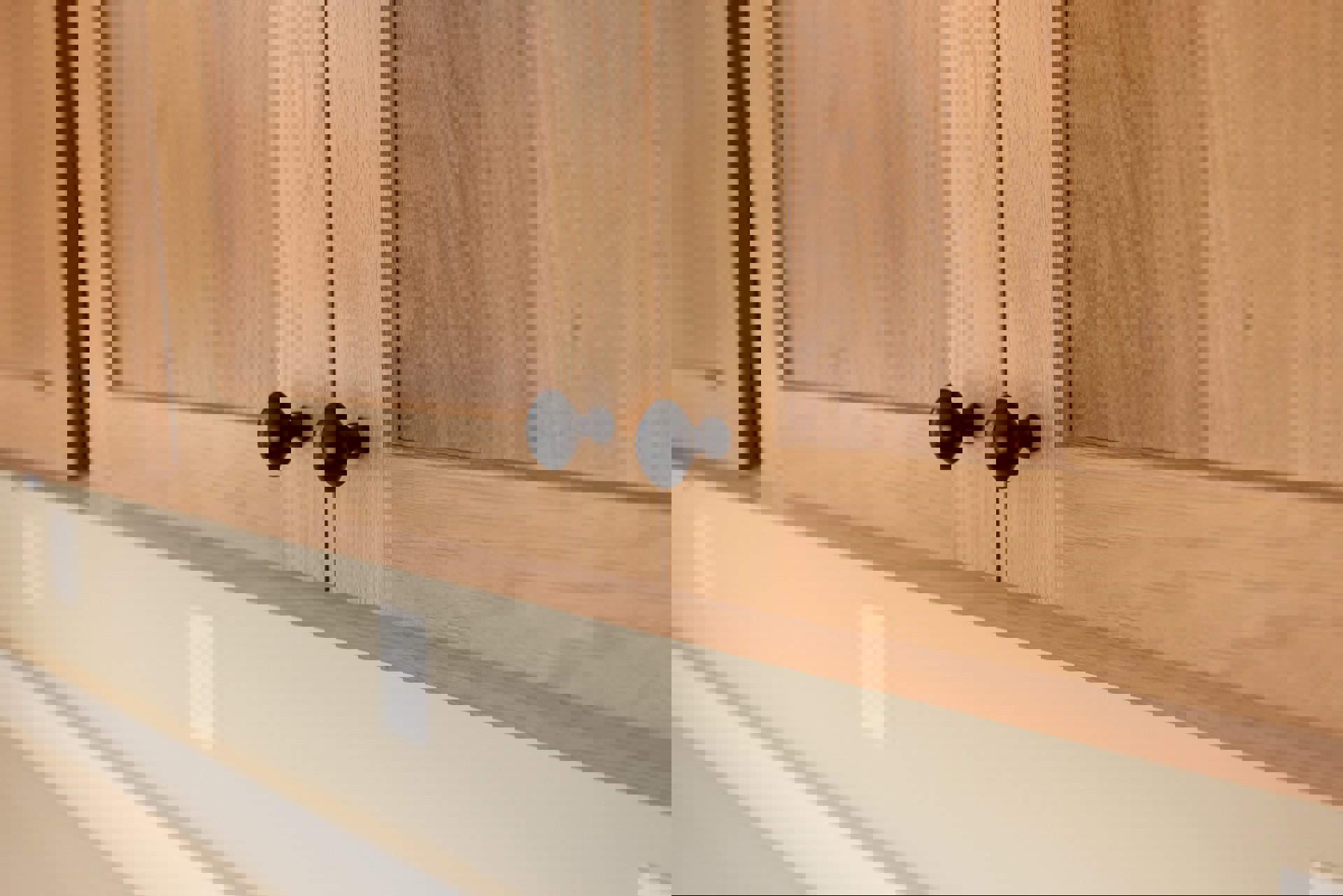 Black metal door knob mounted on light hardwood cabinet door with smooth varnished finish, adjacent to white painted wall