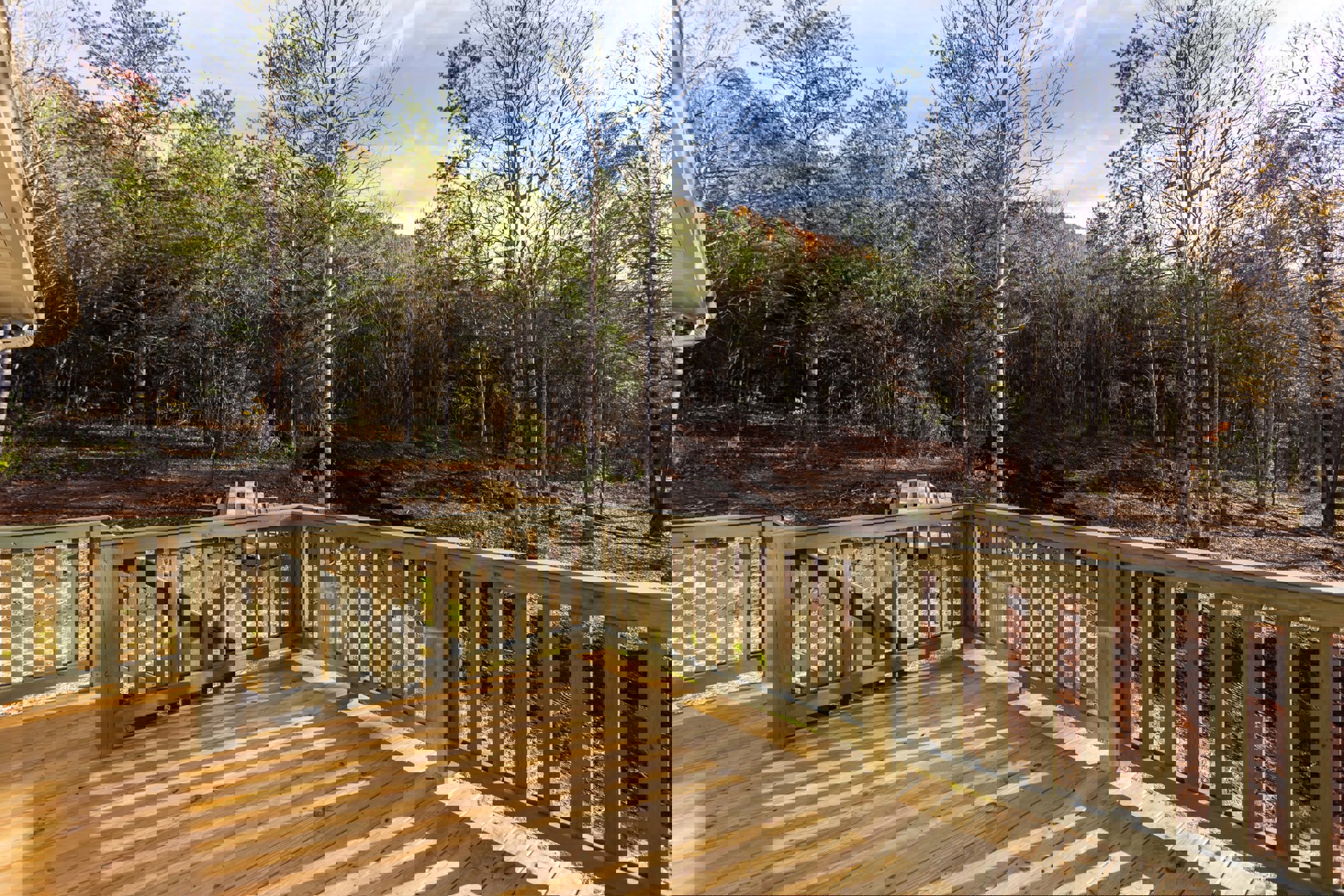 Wooden deck with railing overlooking leafless trees, stacked firewood beside tree, large window visible on house exterior