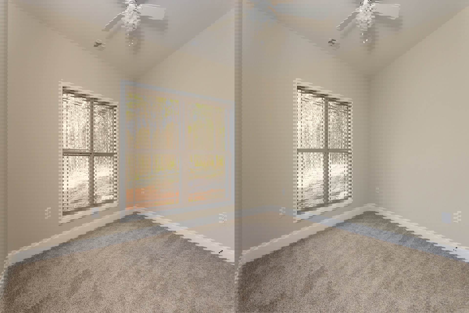 Carpeted room with white ceiling fan and light fixture, large window overlooking green trees, white walls and trim