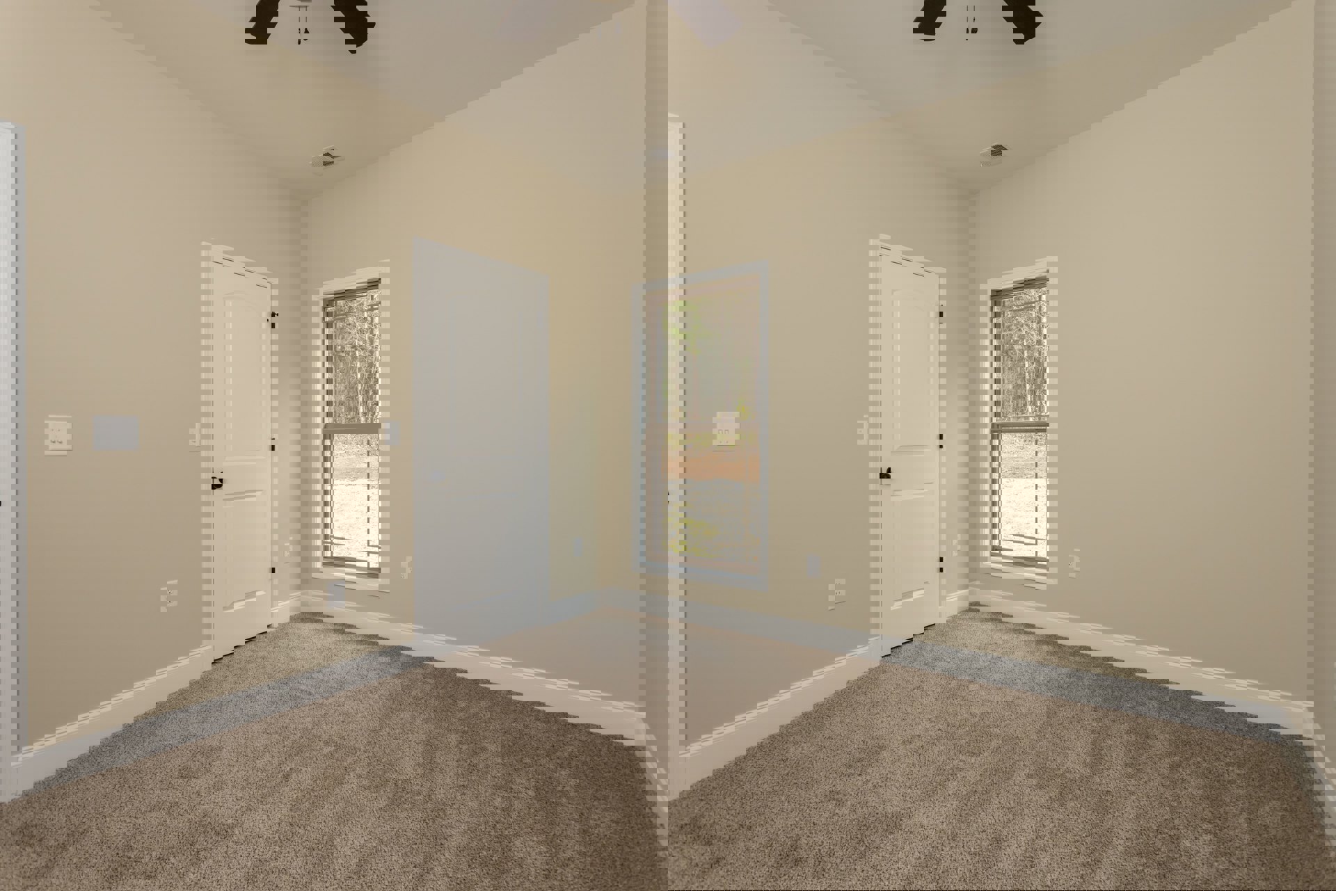 Carpeted room with white walls, ceiling fan, large window showing trees and grass outside, white door with black knob