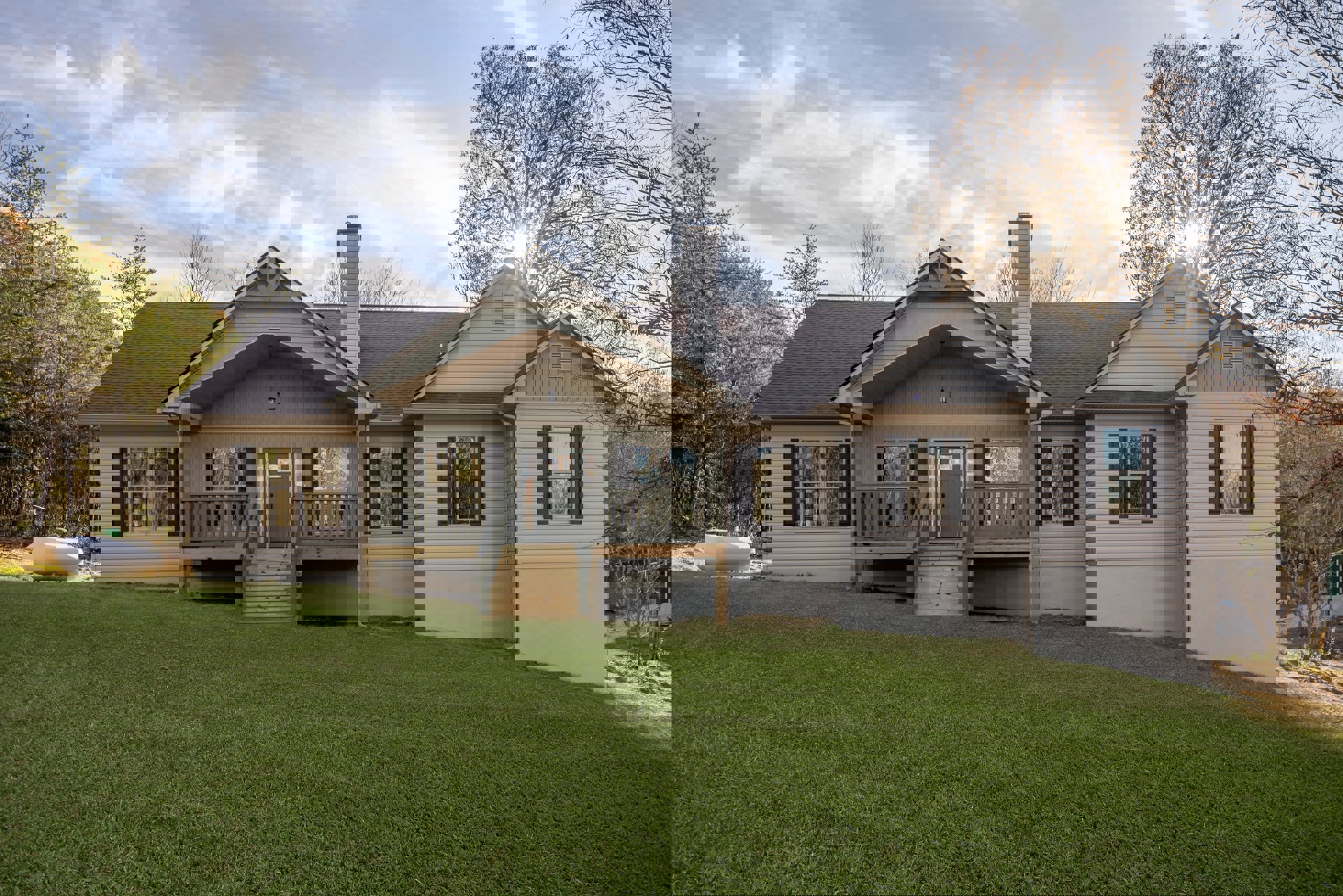 Two-story home with white siding, black shuttered windows, covered front porch with wooden columns, manicured green lawn, and mature trees in the background