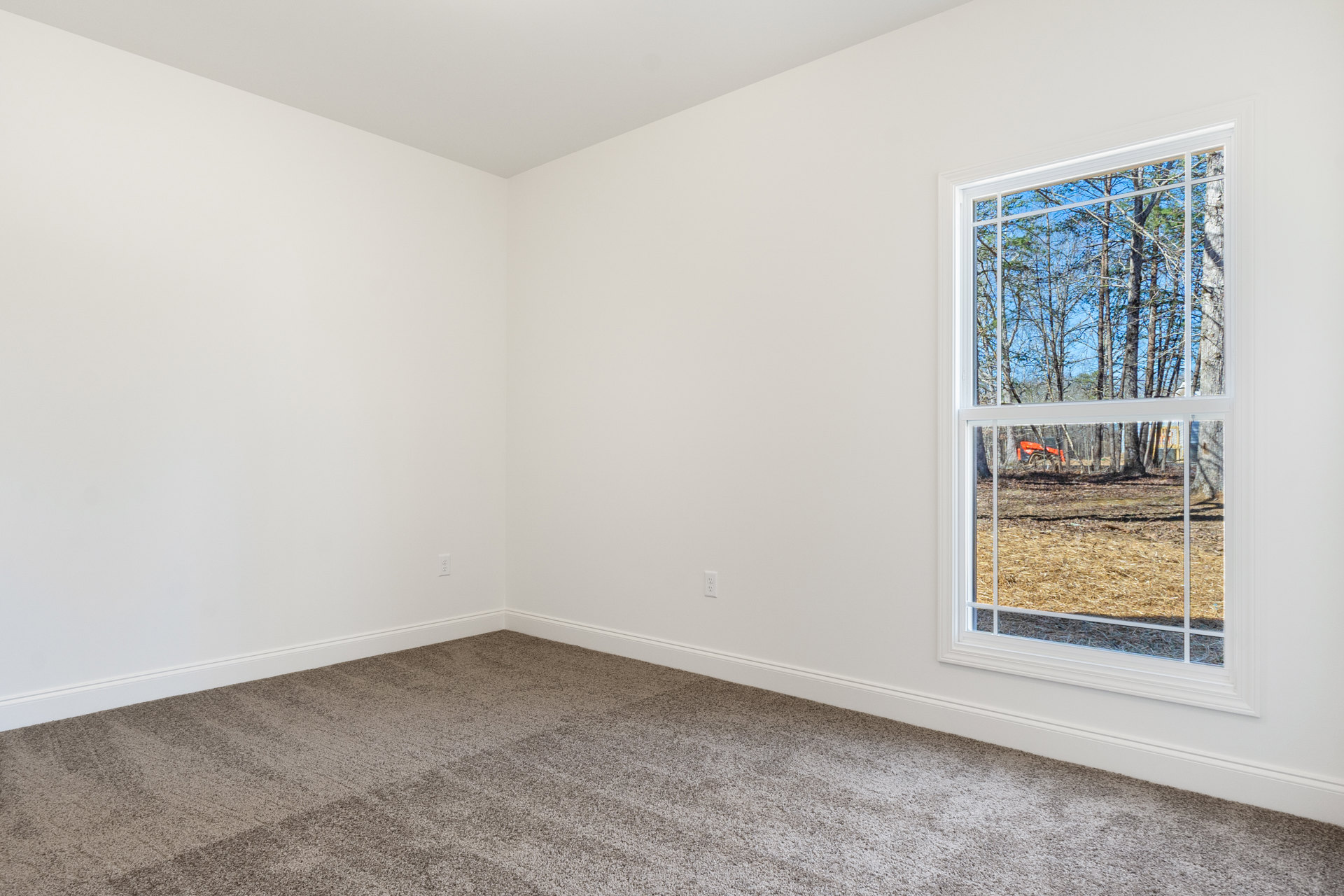 Carpeted room with white plaster walls, large window overlooking red tractor and wooded landscape