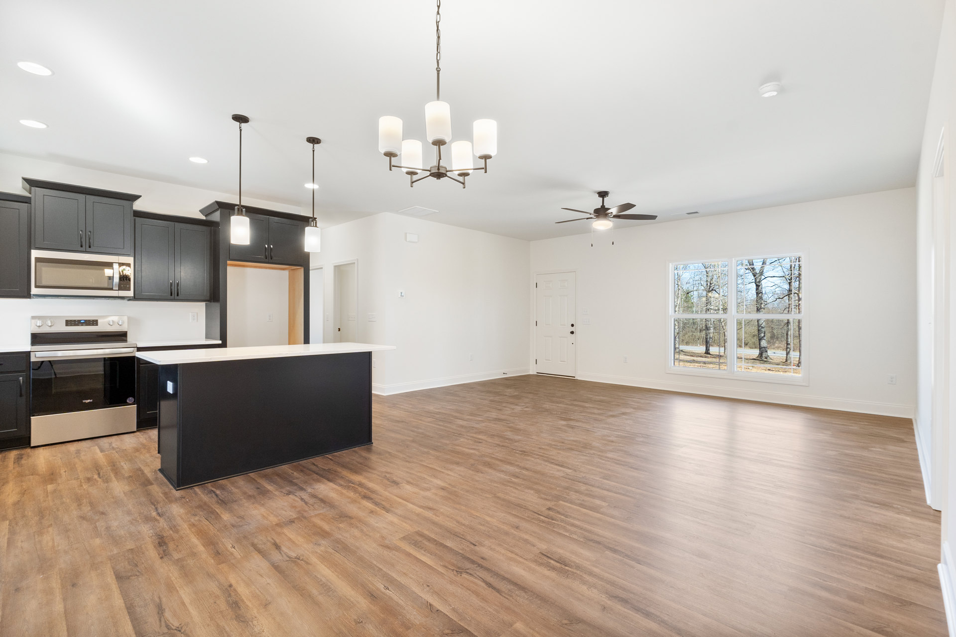 Kitchen with wood flooring, central island featuring black cabinetry and white countertop, stainless steel stove with glass door, white microwave mounted above, large window